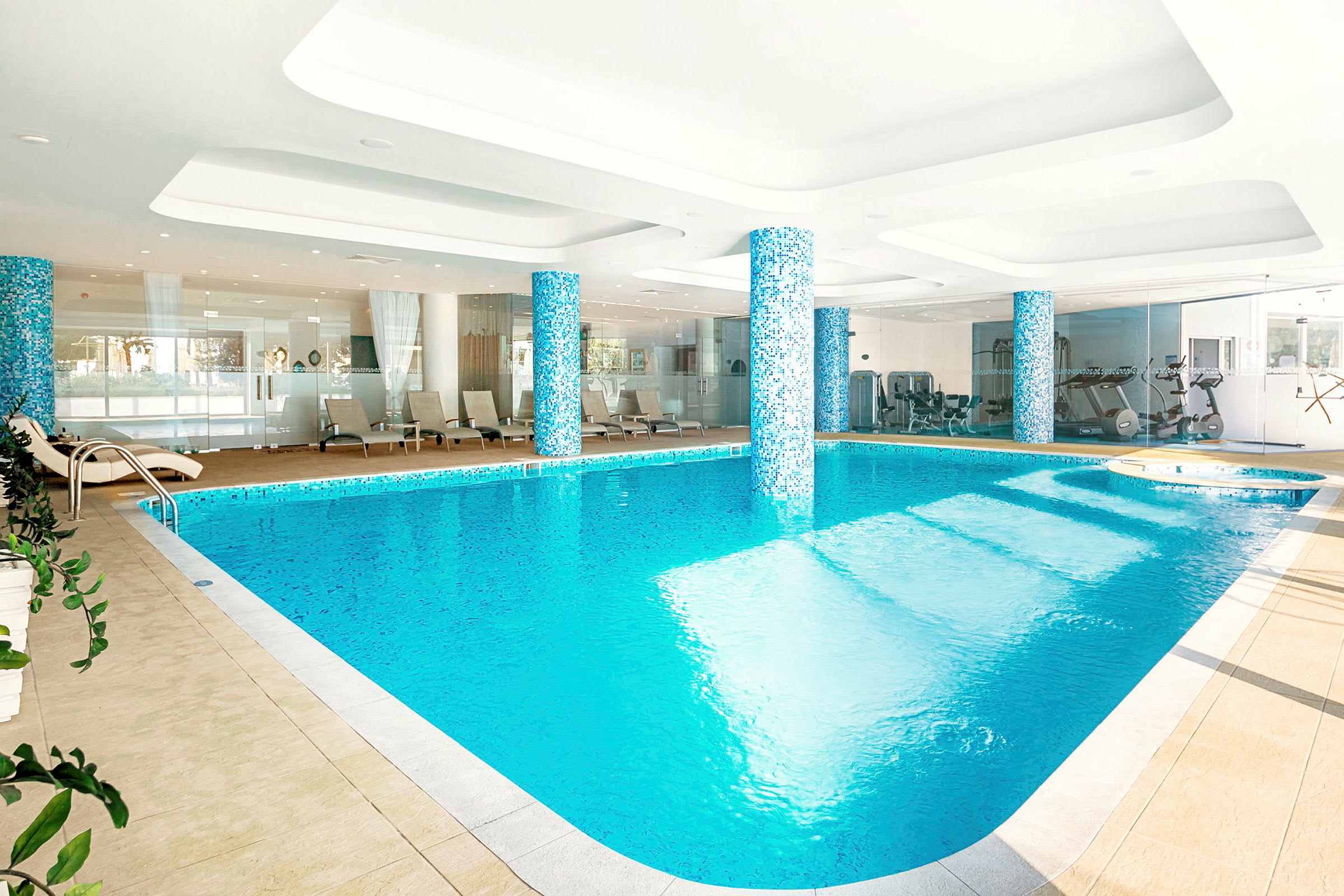 Indendørs pool med omkringliggende afslapningsområde og fitnessudstyr i baggrunden. (AI-genereret tekst)