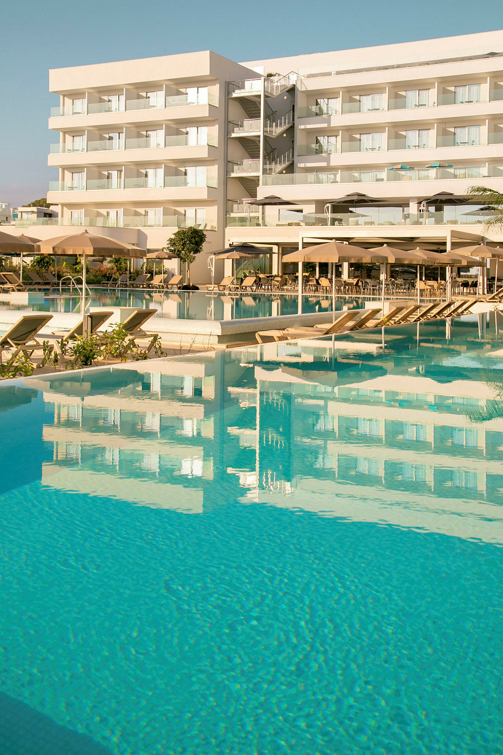 Hotel med poolområde, der reflekteres i vandet. (AI-genereret tekst)