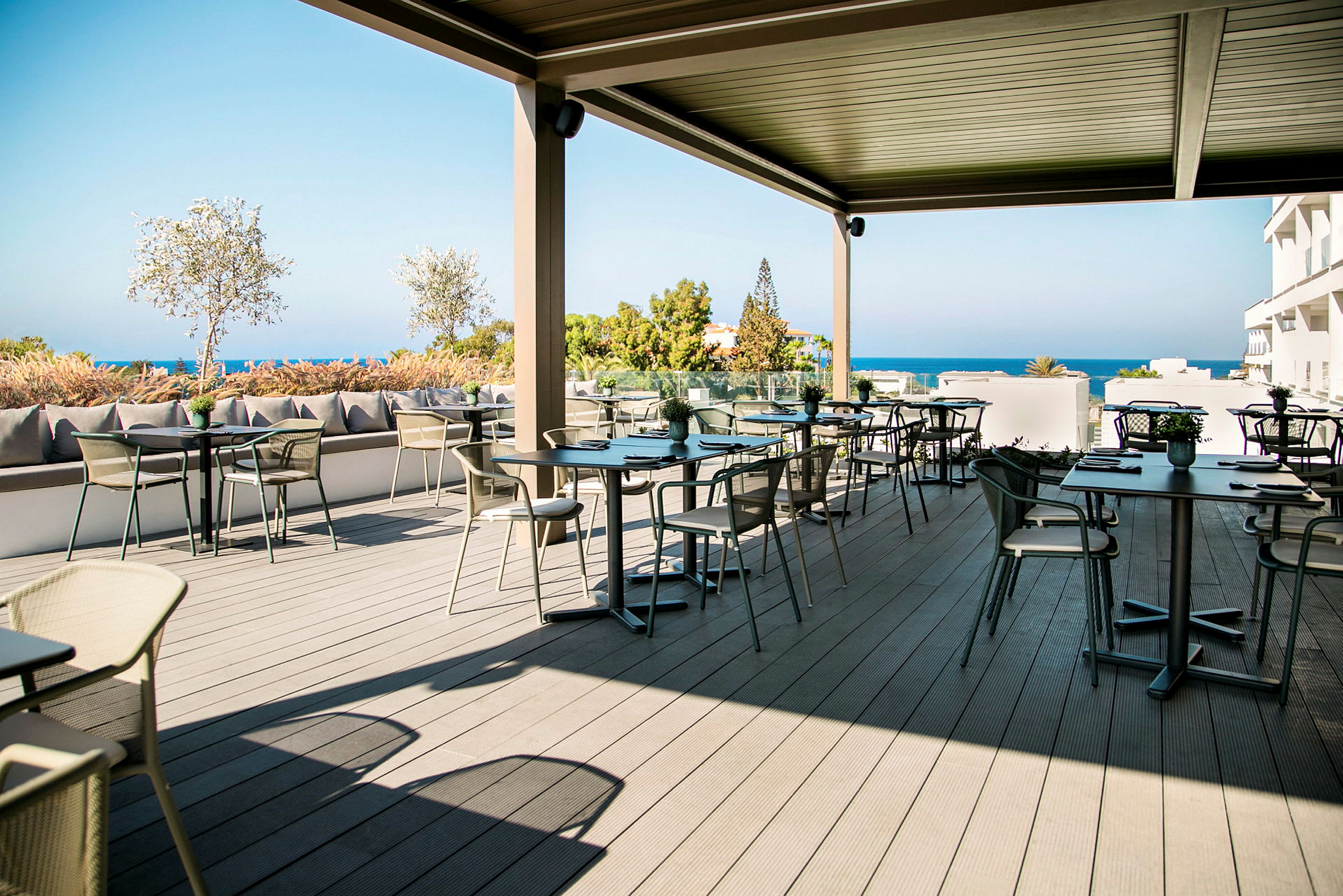 En udendørs café med borde og stole på en terrasse med udsigt over havet. (AI-genereret tekst)