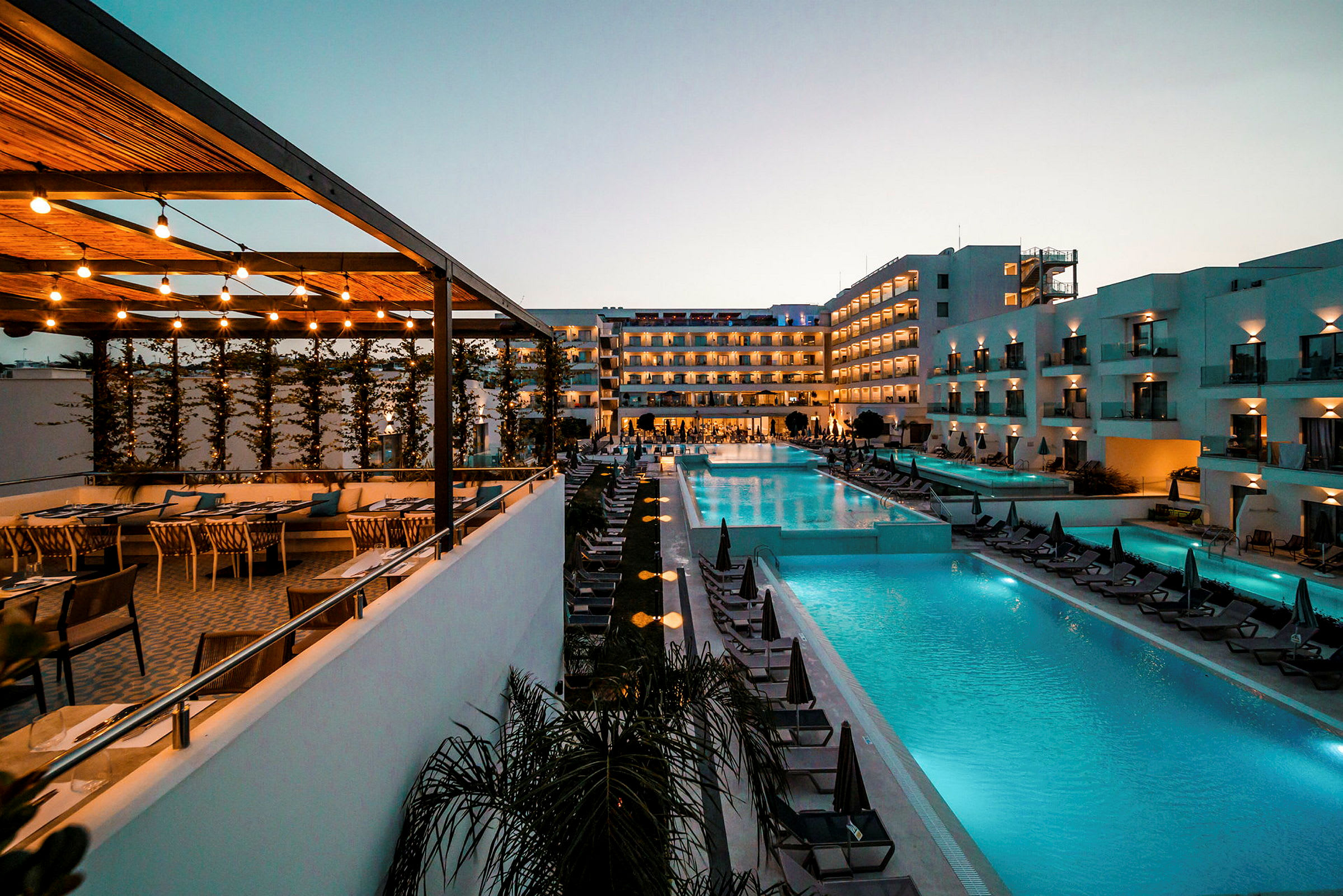 Billede af et hotelområde med pool og siddepladser ved solnedgang. (AI-genereret tekst)