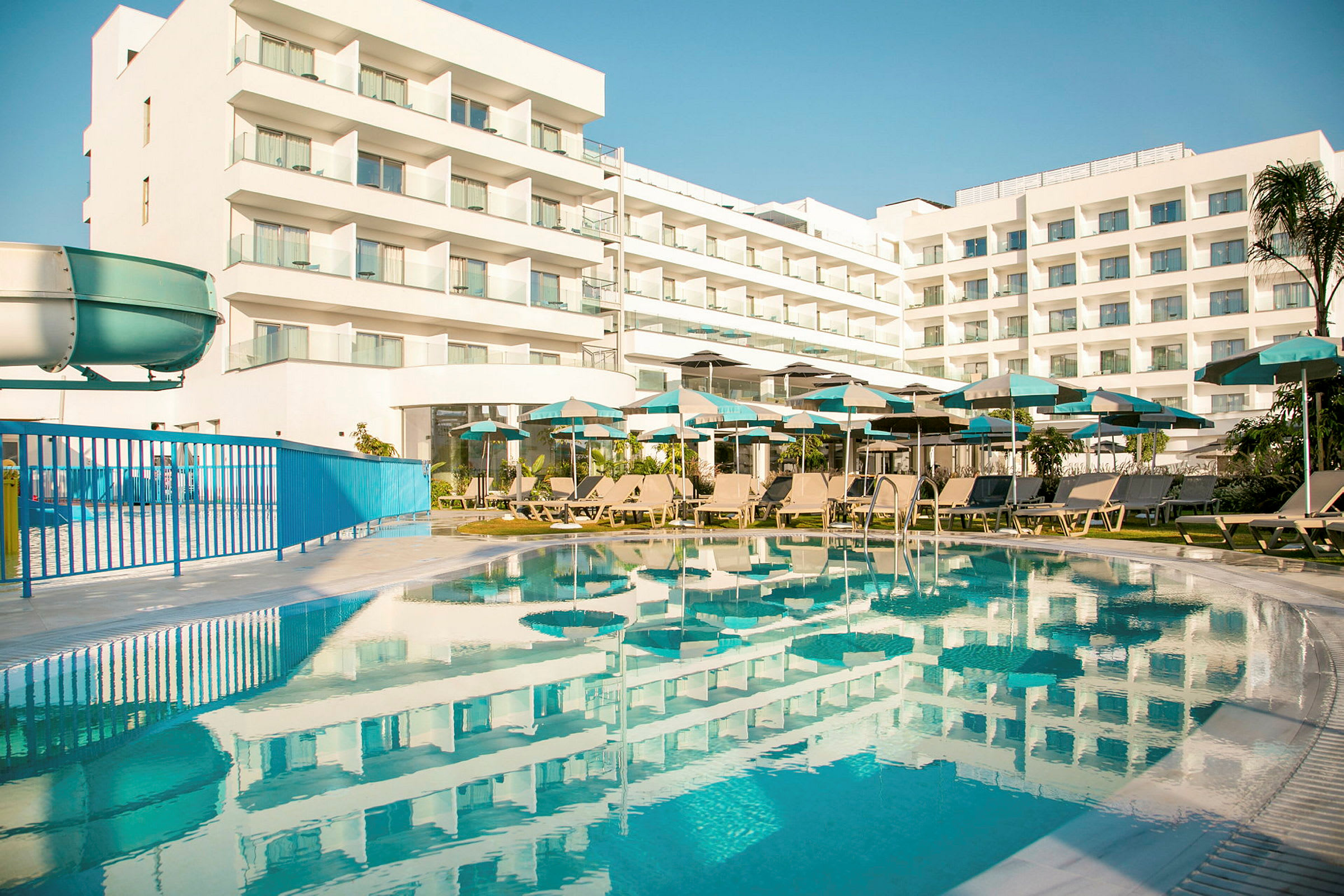 Hotelbygning med altaner og en swimmingpool i forgrunden. (AI-genereret tekst)