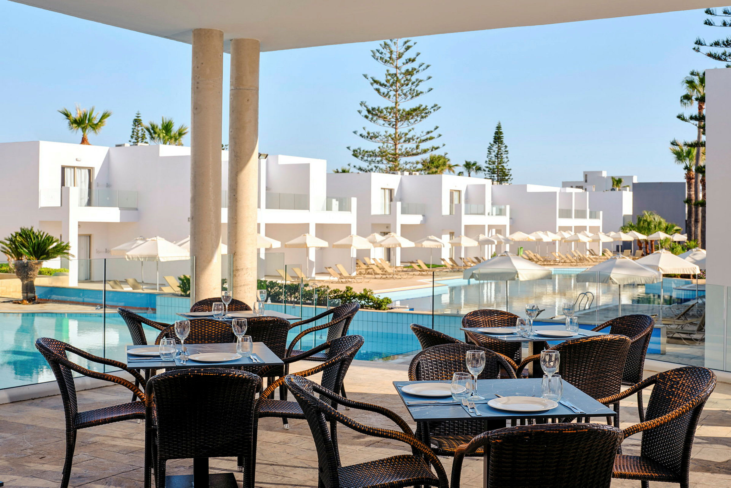 Restaurant med borde og stole ved en terrasse med poolområde. (AI-genereret tekst)