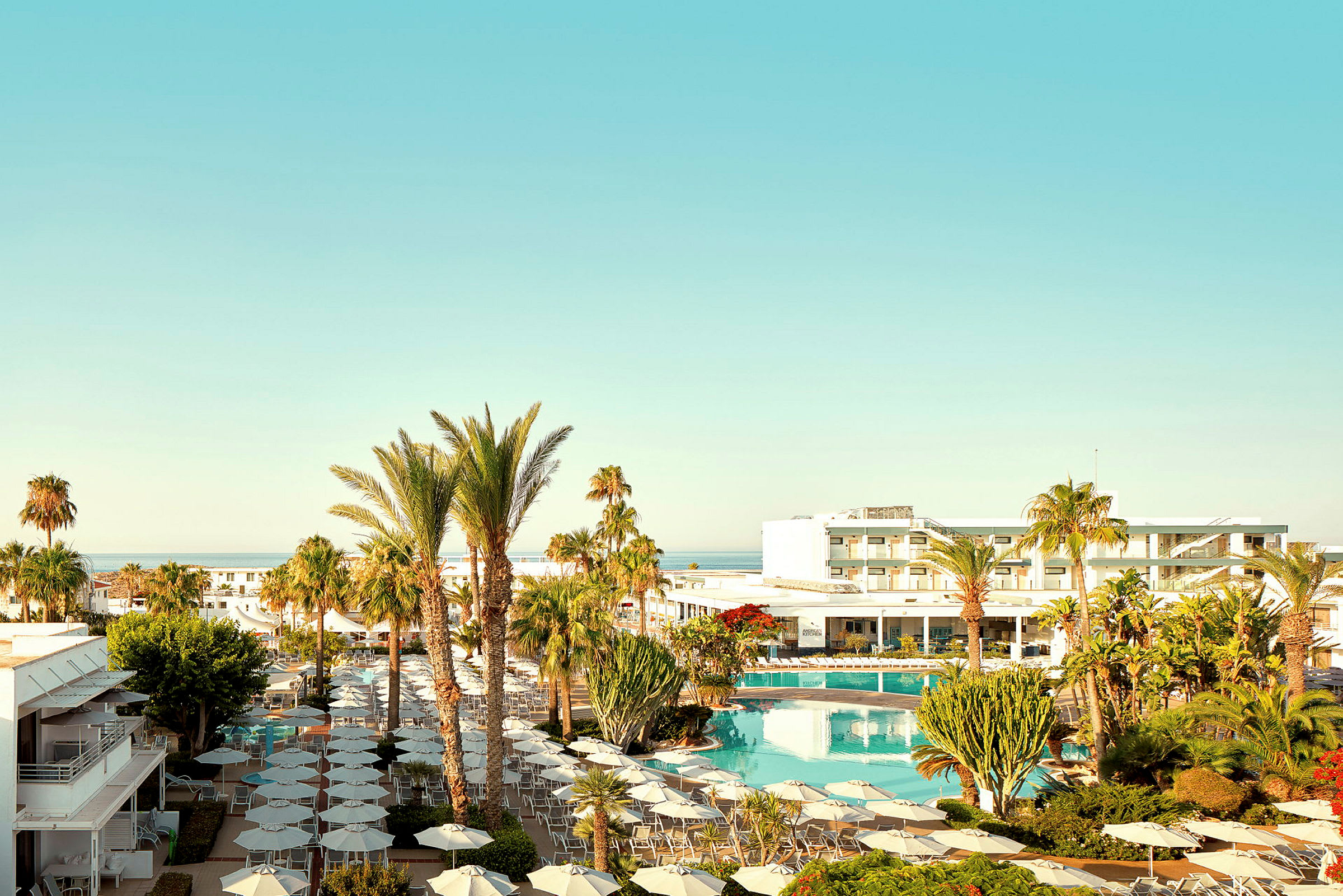 Et hotelområde med pool, parasoller og omgivelser med palmer under en klar blå himmel. (AI-genereret tekst)