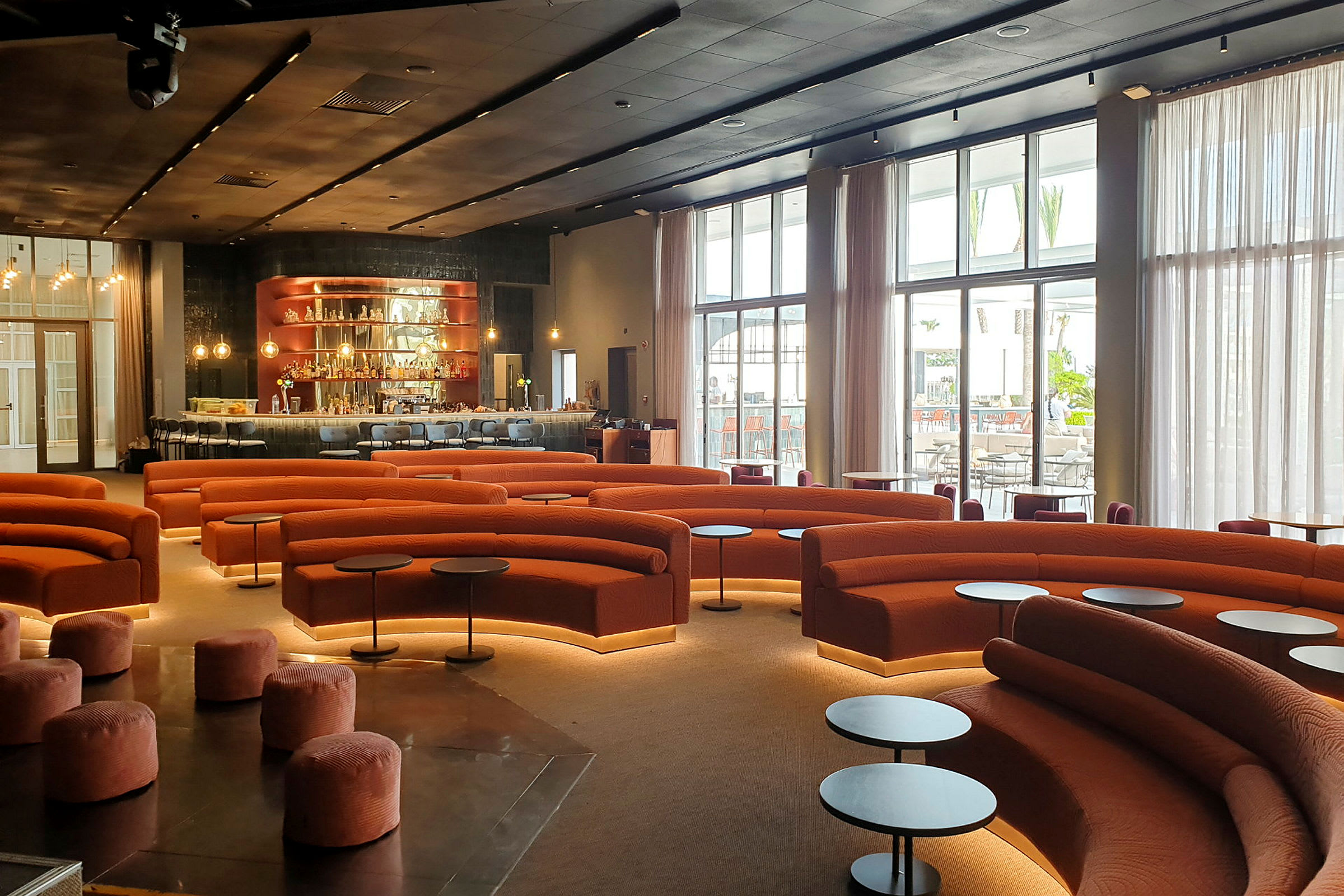En moderne lounge med orange sofaer, runde småborde og en bardisk i baggrunden. (AI-genereret tekst)
