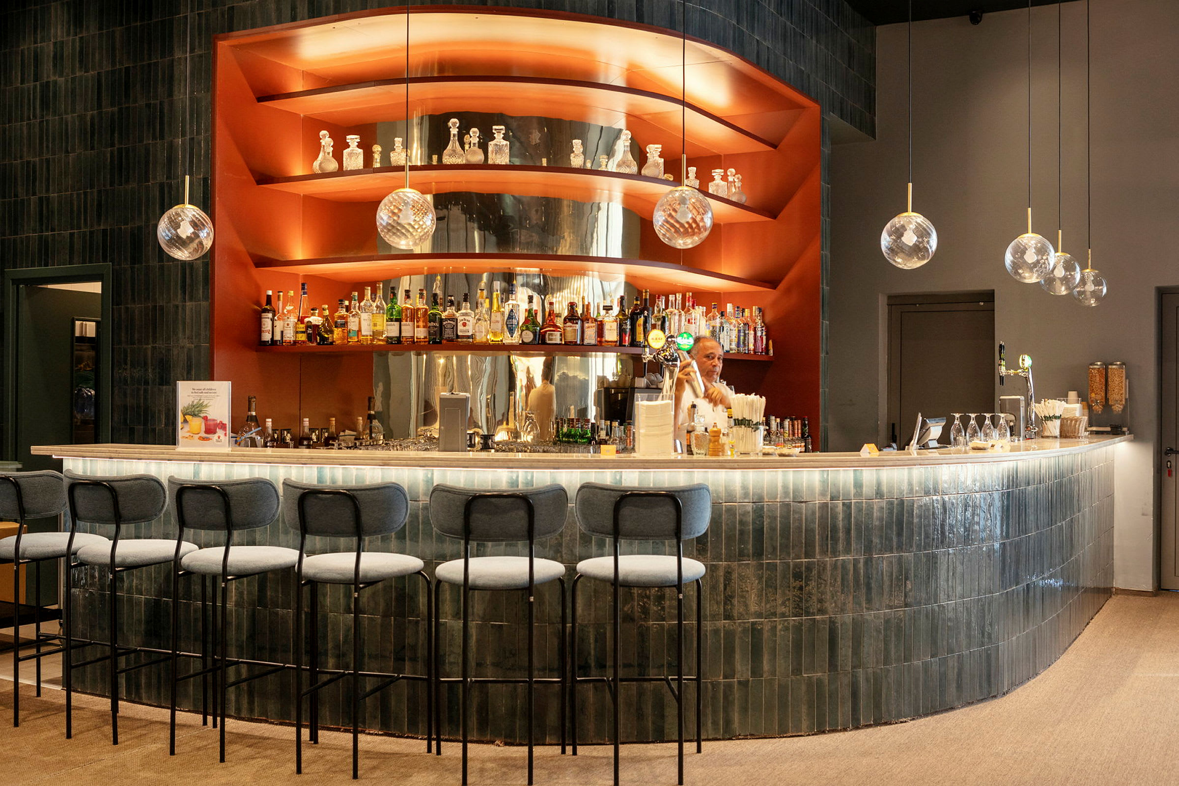 En moderne bar med lys stenklinkebordplade og hylder med spiritusflasker, dekorationer og hængende glaskupler. (AI-genereret tekst)