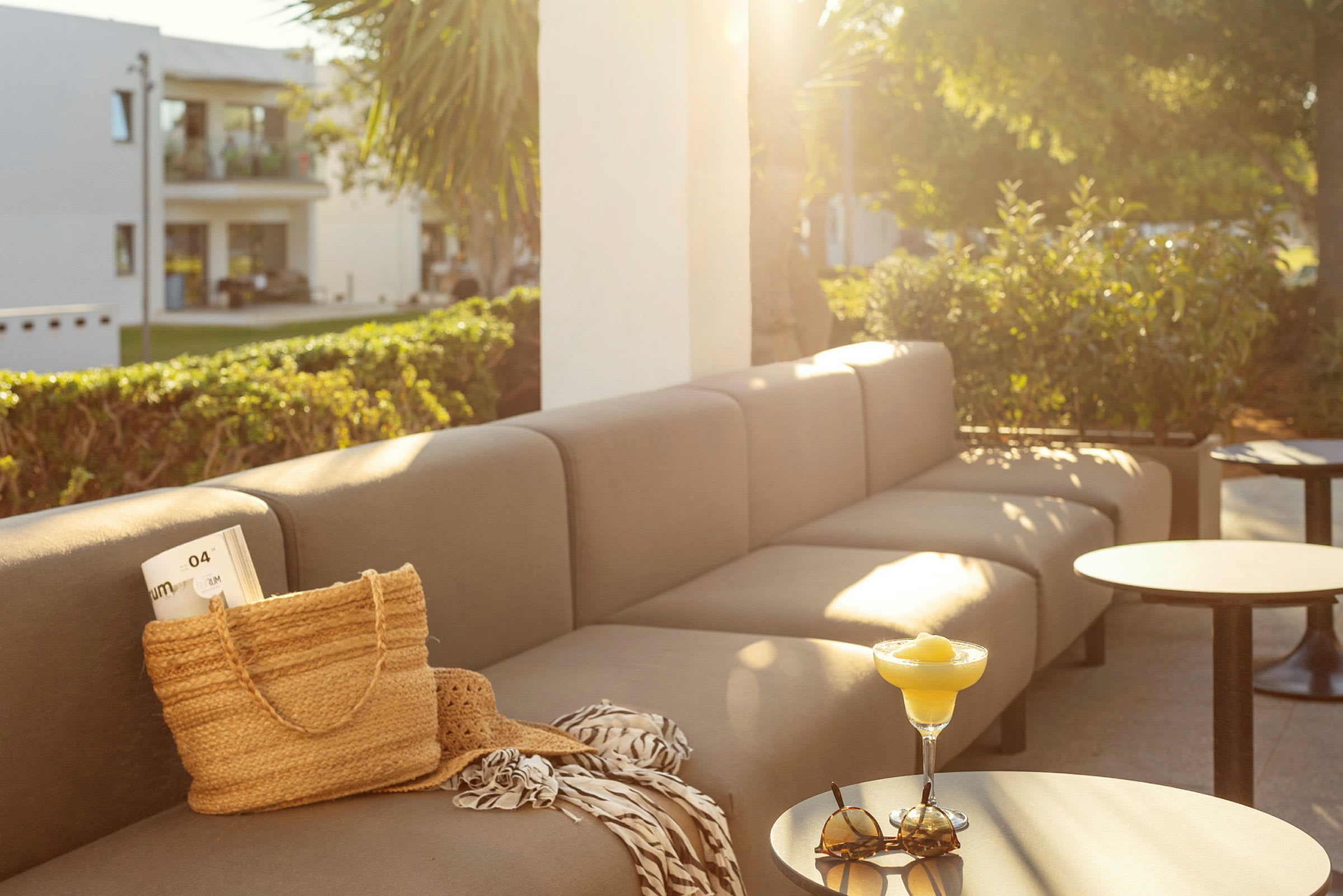 Sofa og bord på en terrasse med sollys, på bordet står et glas og solbriller. (AI-genereret tekst)