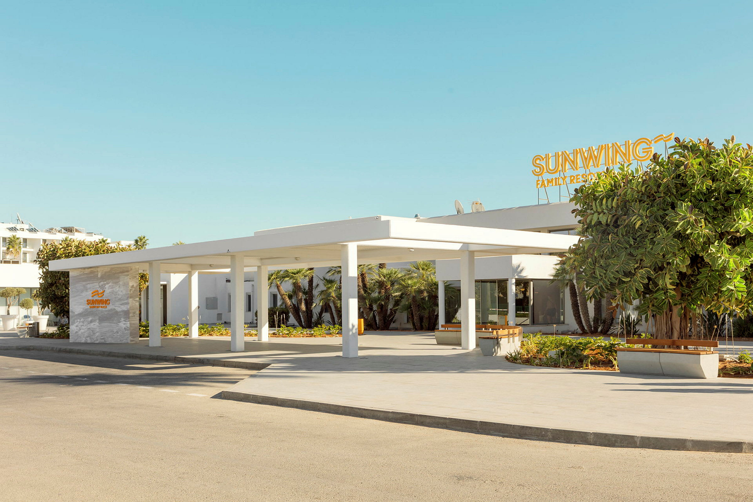 Billede af indgangen til et moderne hotel med en hvid facade og et skilt med teksten Sunwing Family Resort. (AI-genereret tekst)