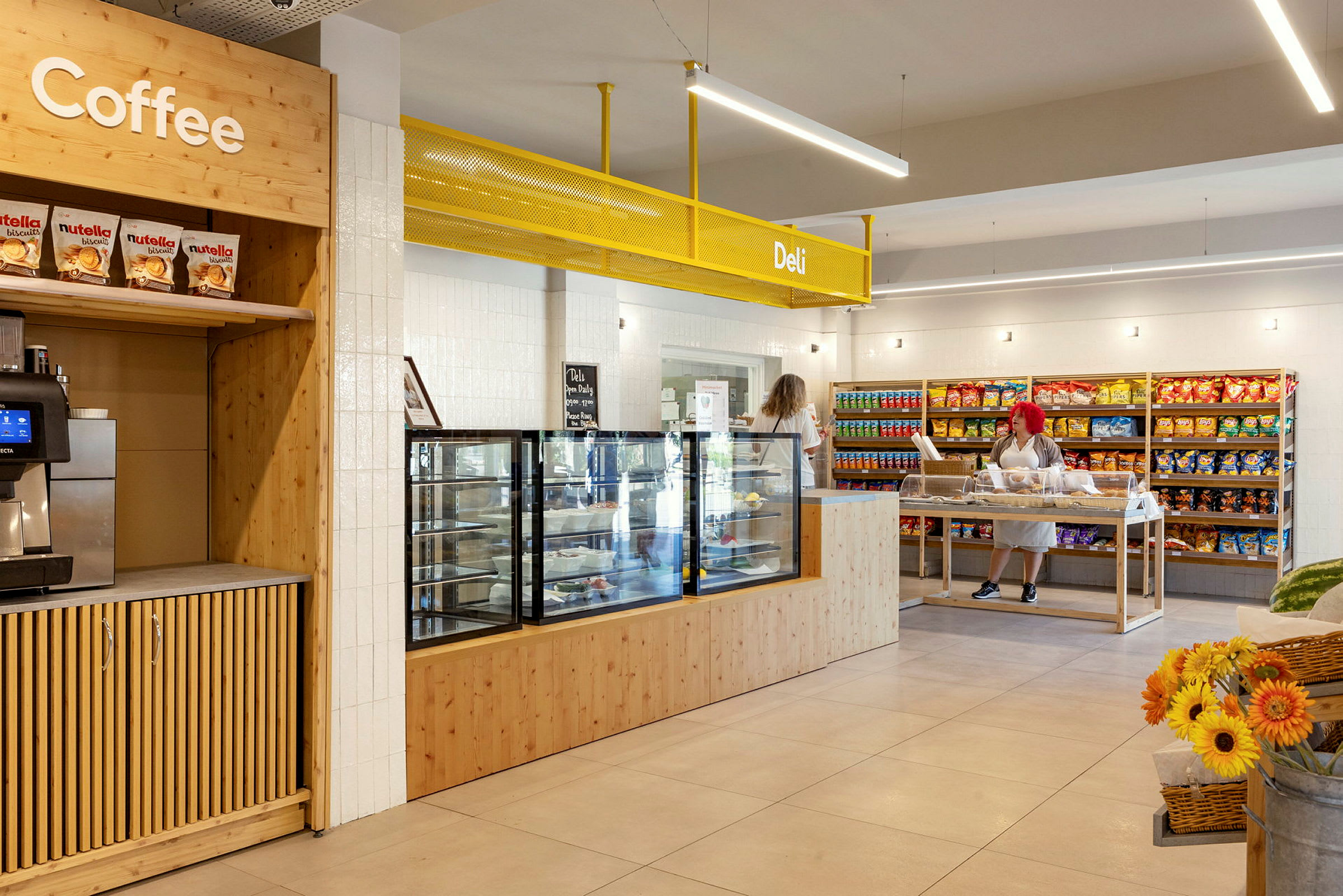 En butiksinteriør med en kaffestation, en disk til sandwich og snacks, samt hylder fyldt med varer. (AI-genereret tekst)