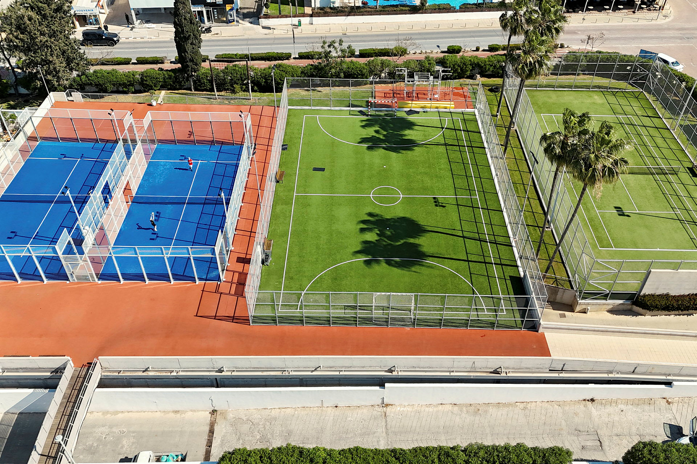 Billede af flere udendørsbaner, herunder en blå tennis- eller padelbane og en grøn fodboldbane. (AI-genereret tekst)