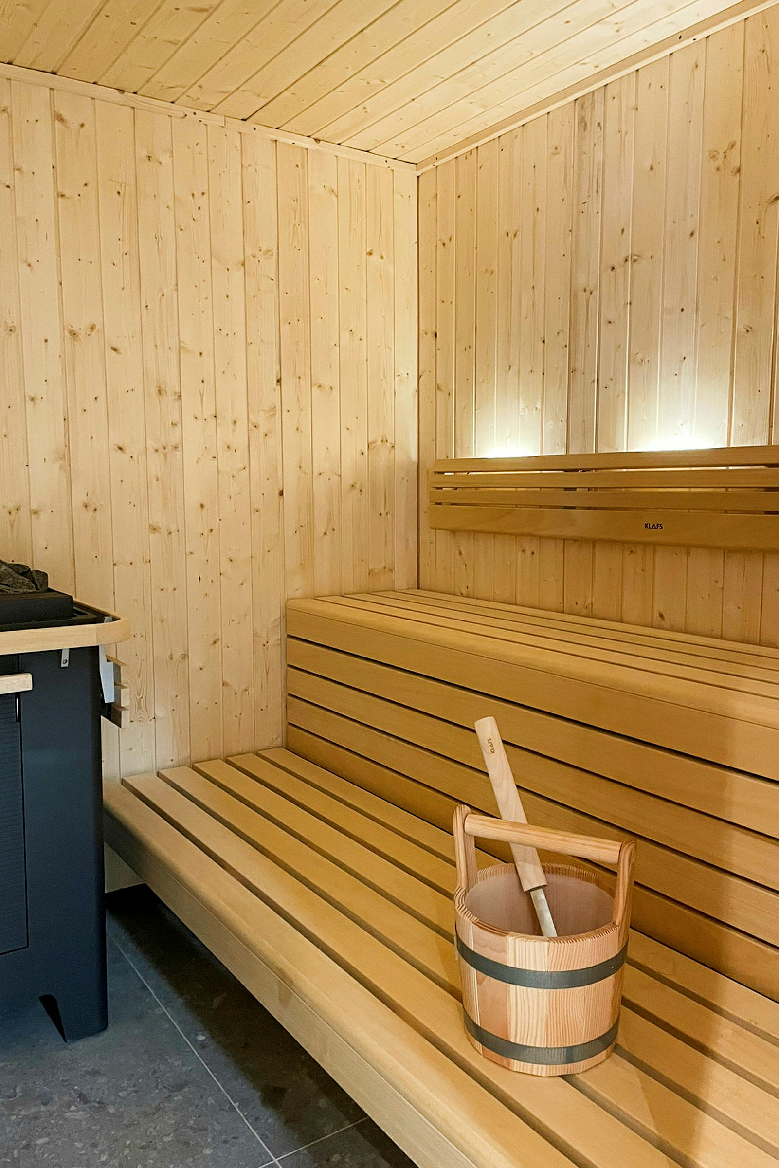 En sauna med træpaneler, en træbænk og en spand med øse til damp. (AI-genereret tekst)