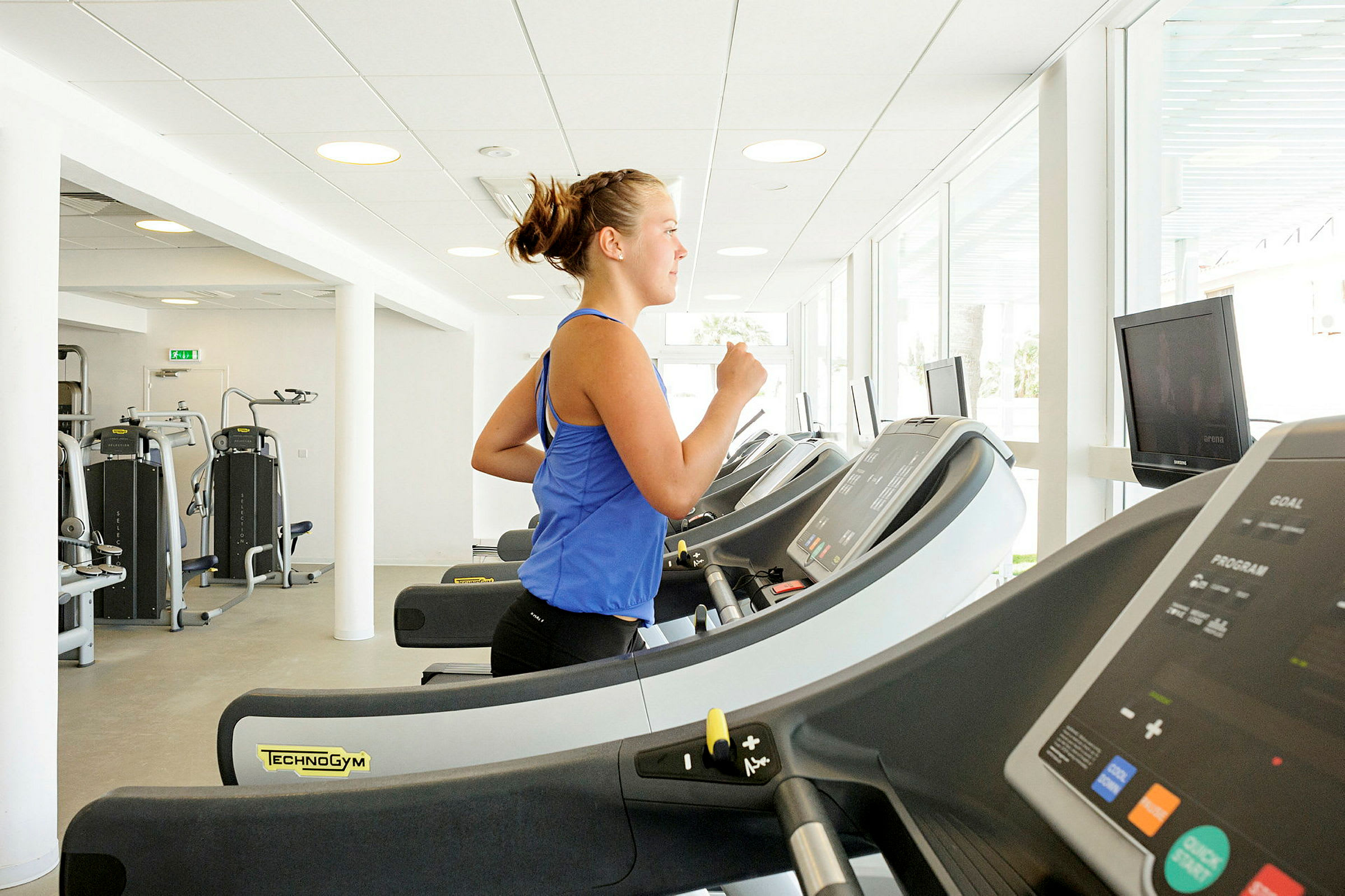 En person træner på et løbebånd i et lyst fitnesscenter. (AI-genereret tekst)