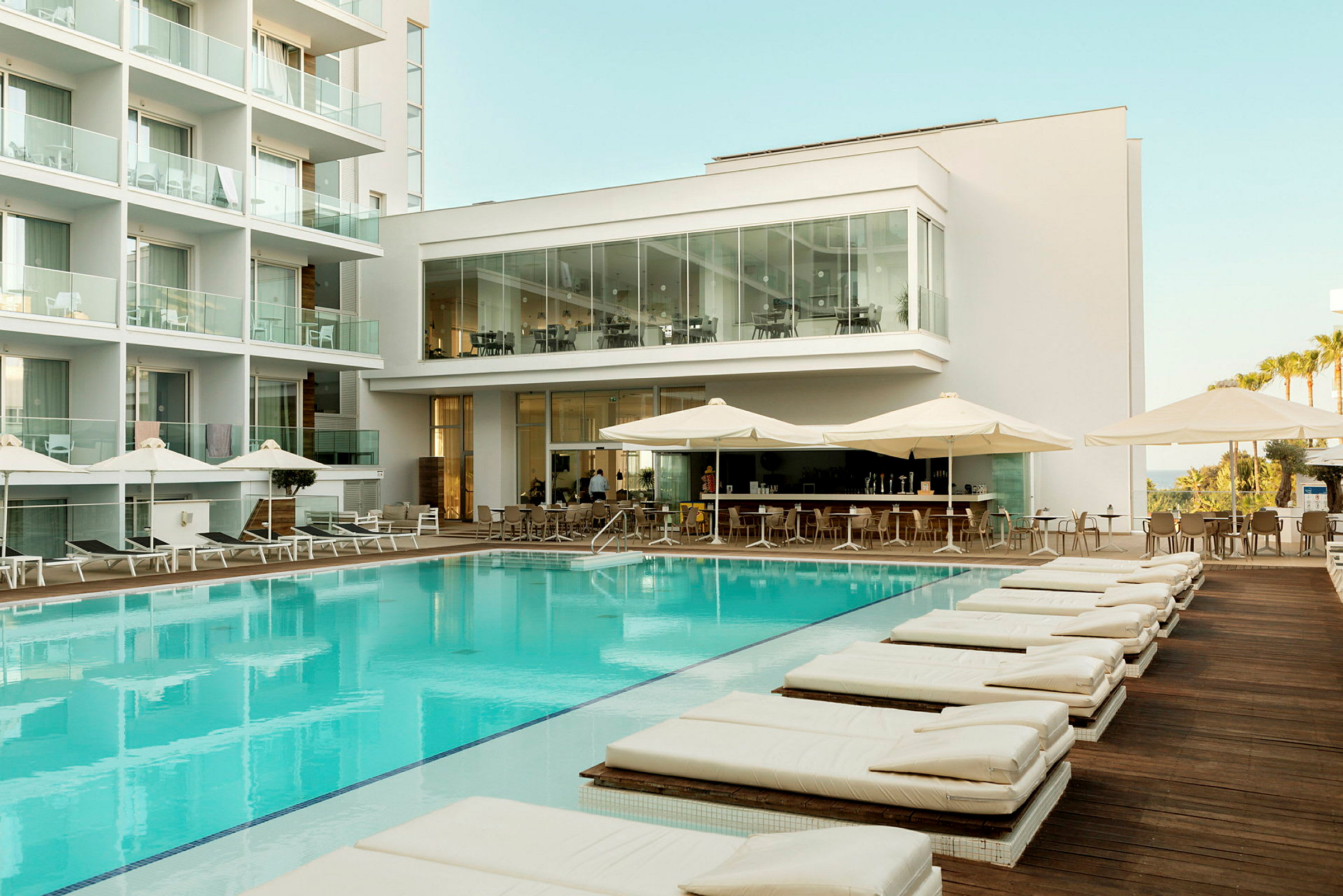 Billede af et hotelområde med pool, liggestole og en udendørsbar. (AI-genereret tekst)