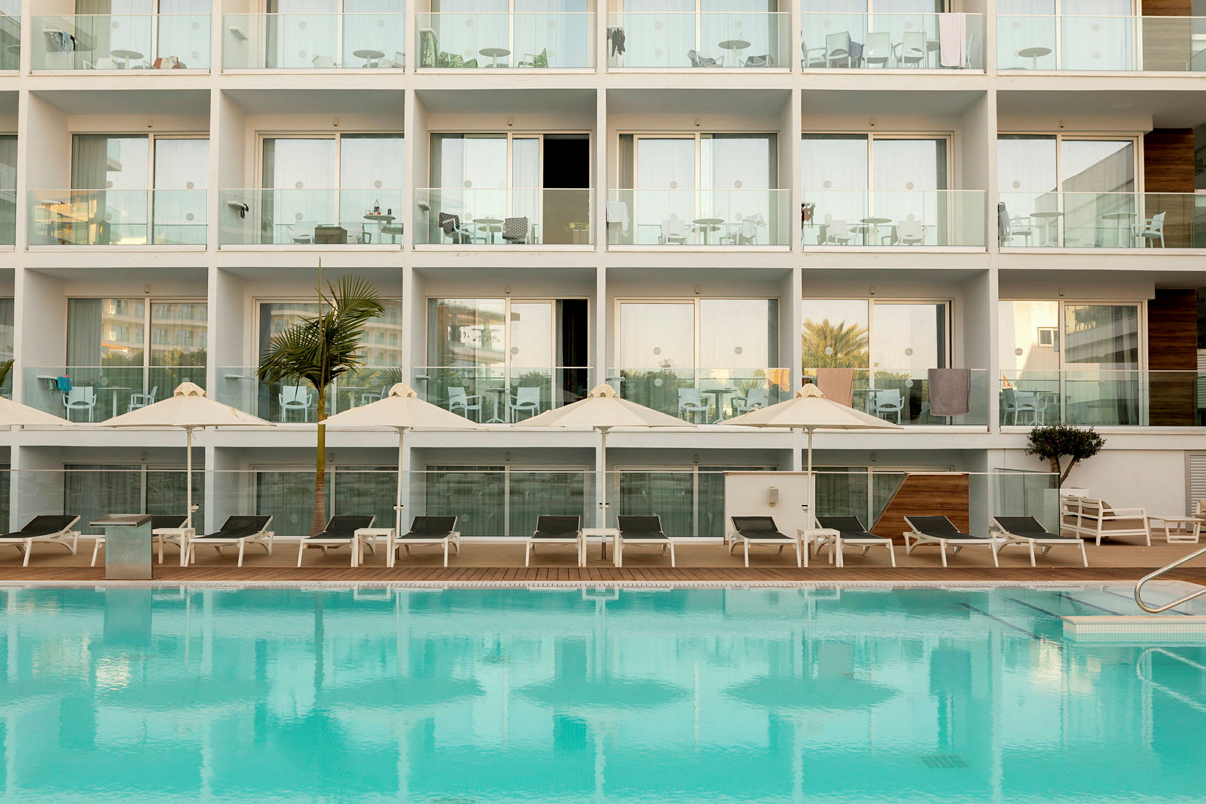 Hotelfacade med altaner og en pool foran. (AI-genereret tekst)