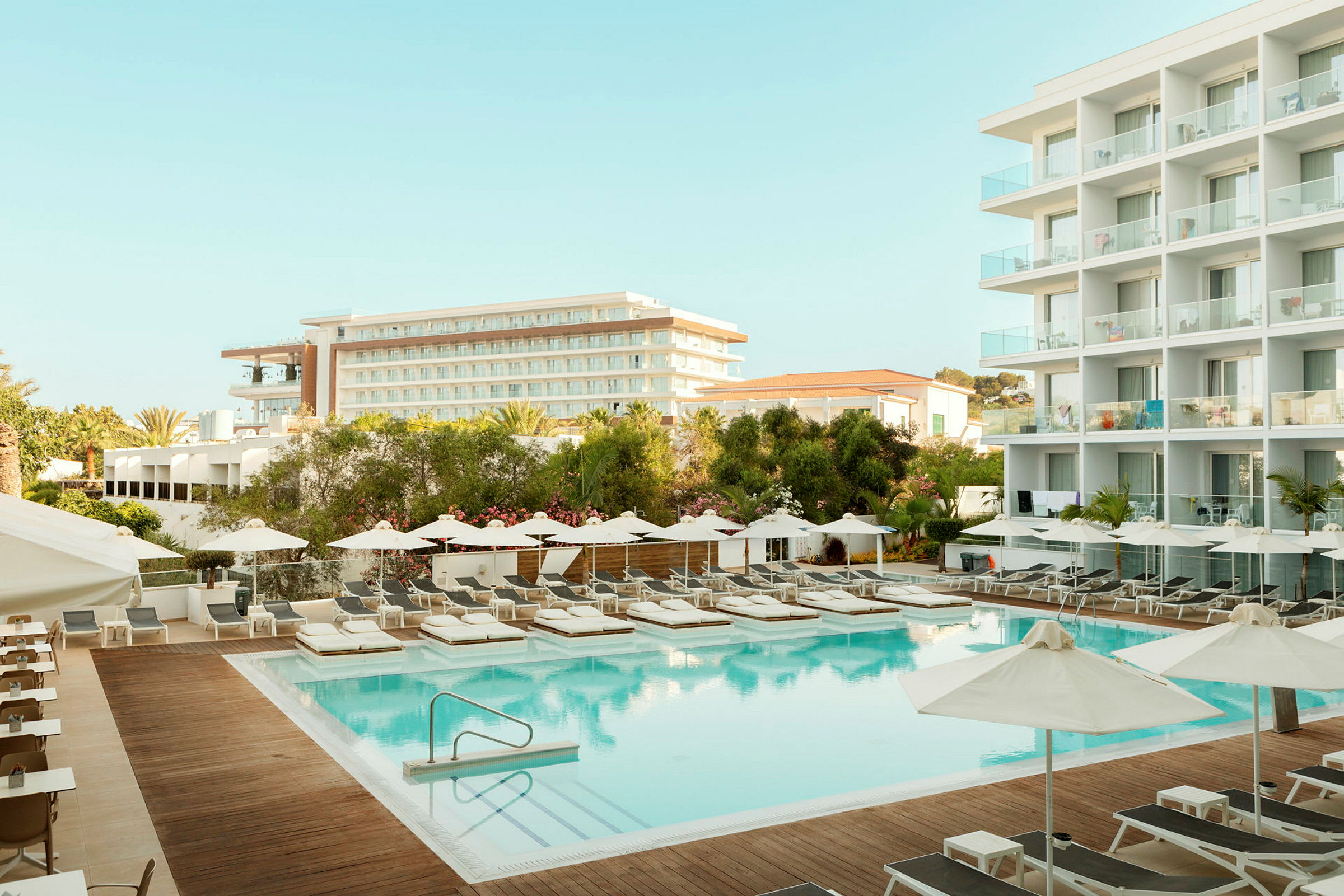 Hotelområde med pool, liggestole og bygninger i baggrunden. (AI-genereret tekst)