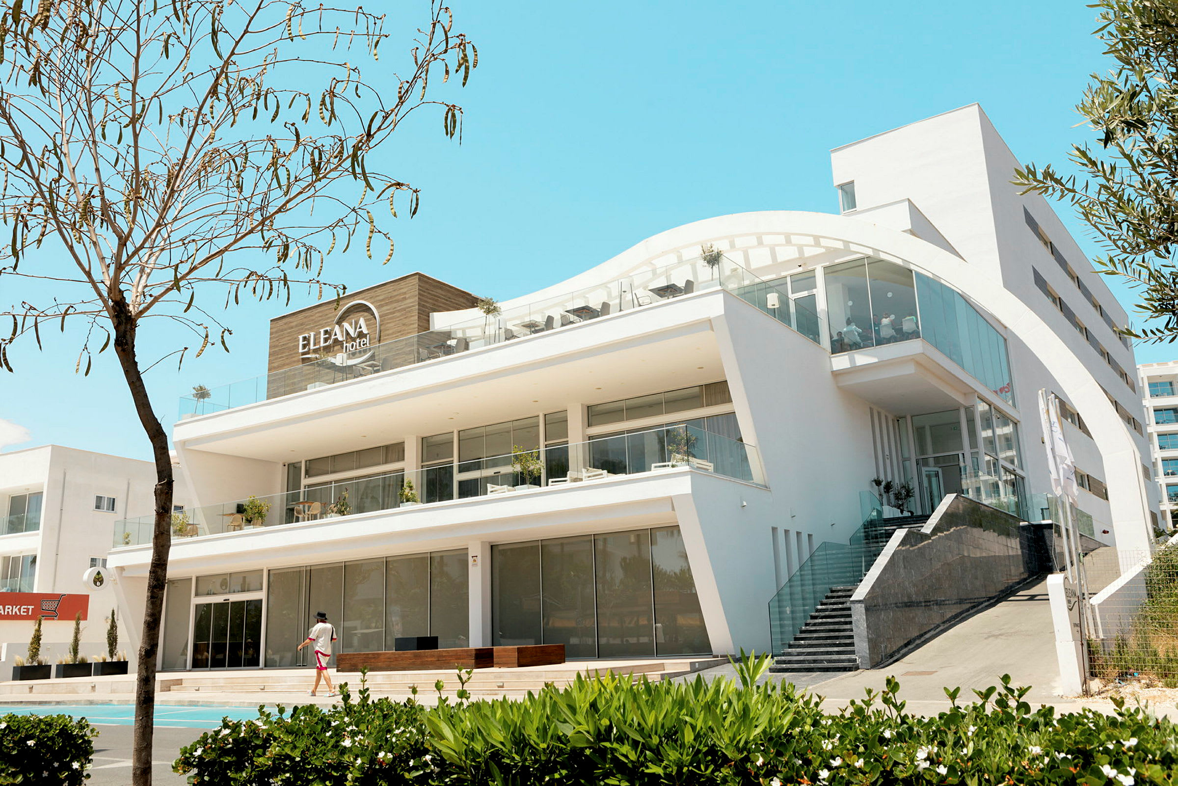 Et moderne hotel med store vinduer og åben design, omgivet af grønne områder. (AI-genereret tekst)