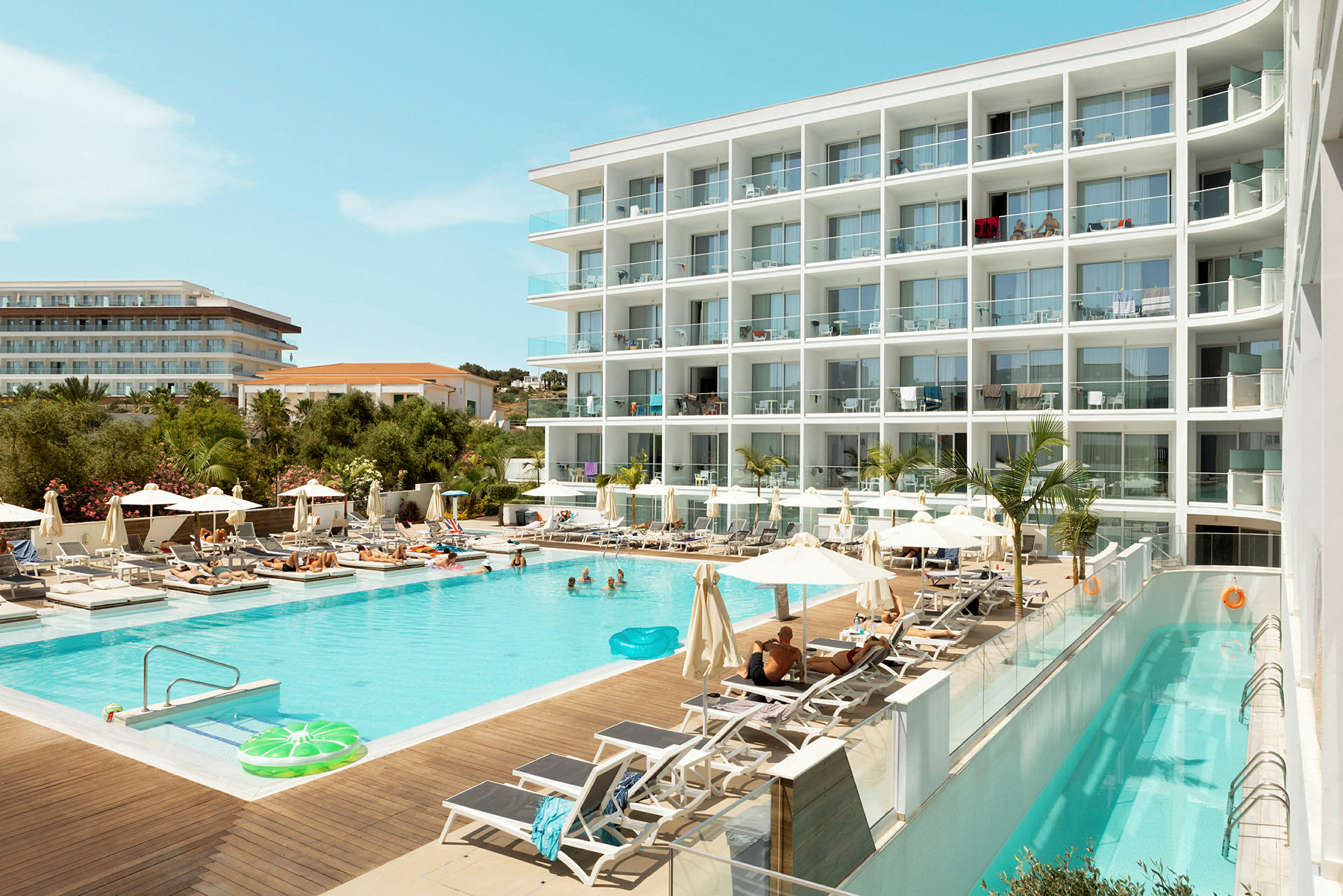 Et hotel med en swimmingpool omgivet af liggestole og parasoller. (AI-genereret tekst)