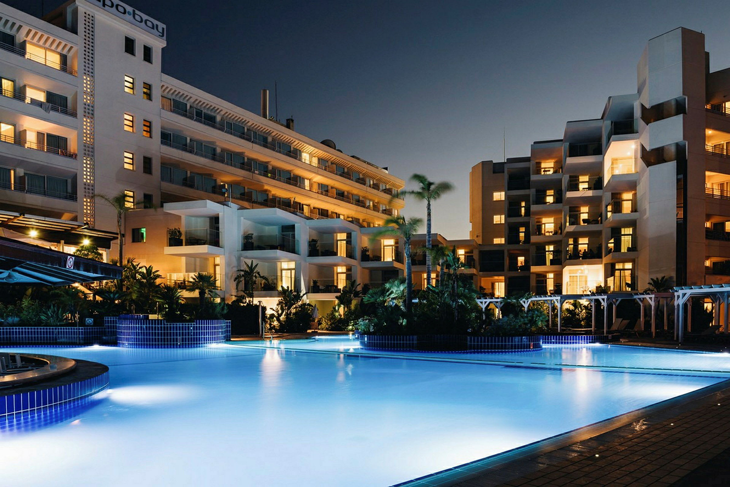 En pool foran hotelbygninger om aftenen. (AI-genereret tekst)