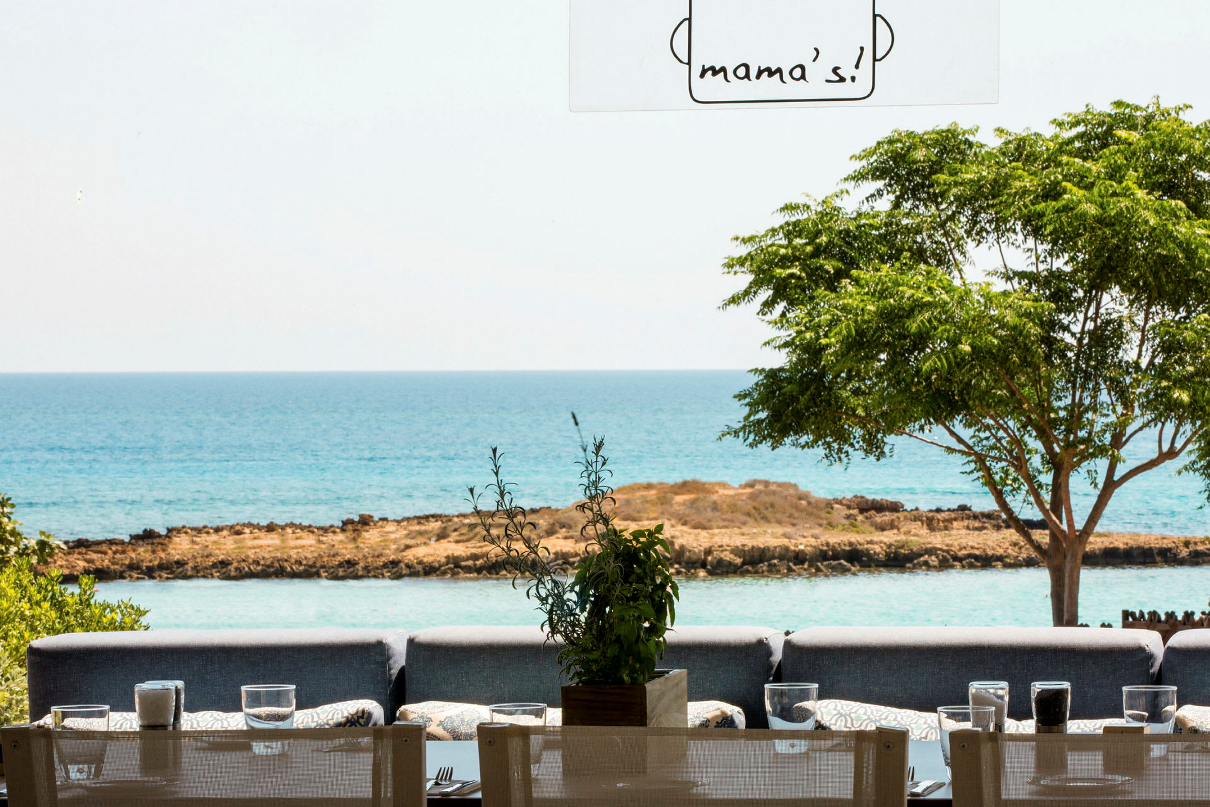 Restaurant med udendørs siddepladser, udsigt til havet og grønt områder. (AI-genereret tekst)