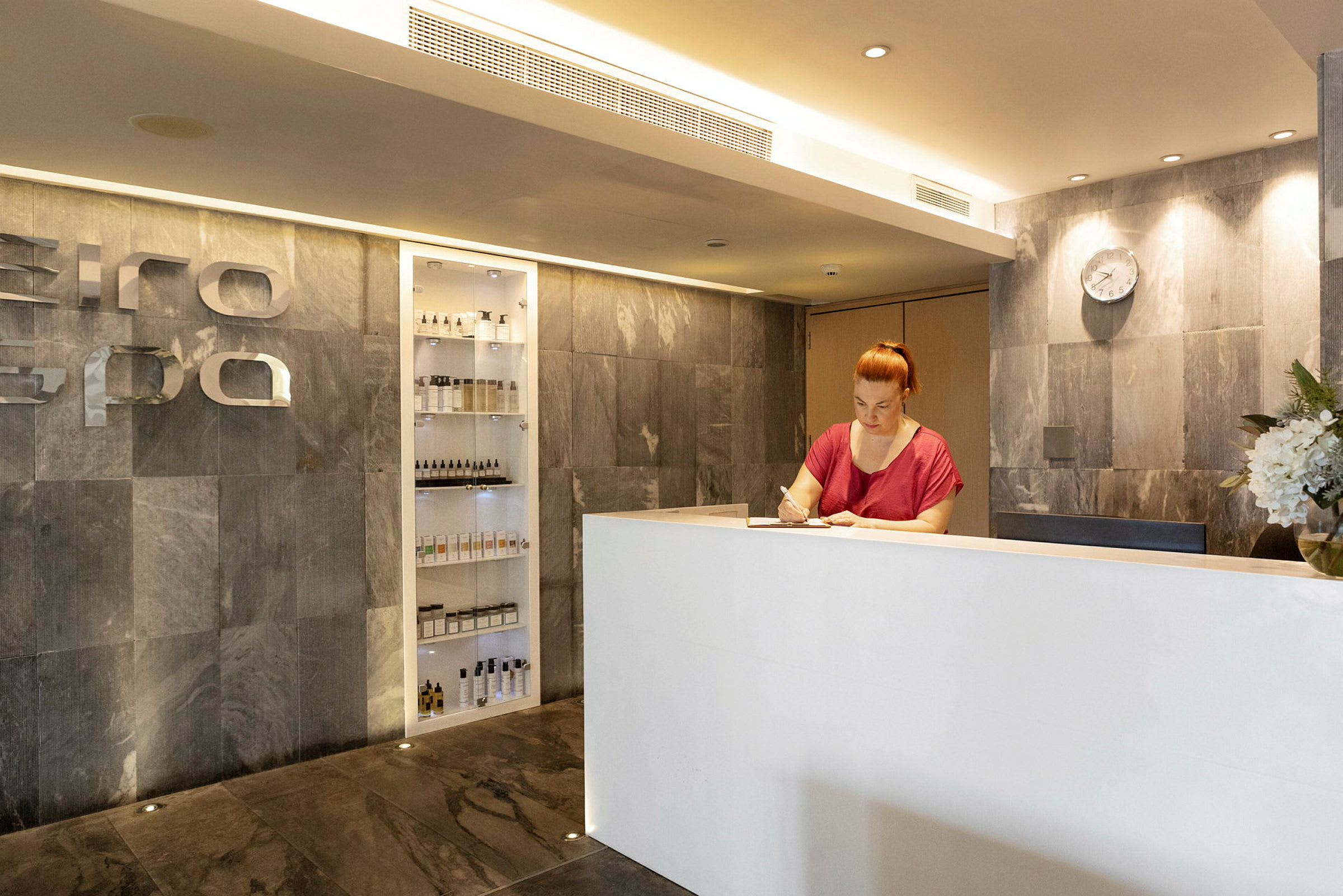 Receptionen i en spa-facilitet med en hvid skranke og vægge af sten. (AI-genereret tekst)