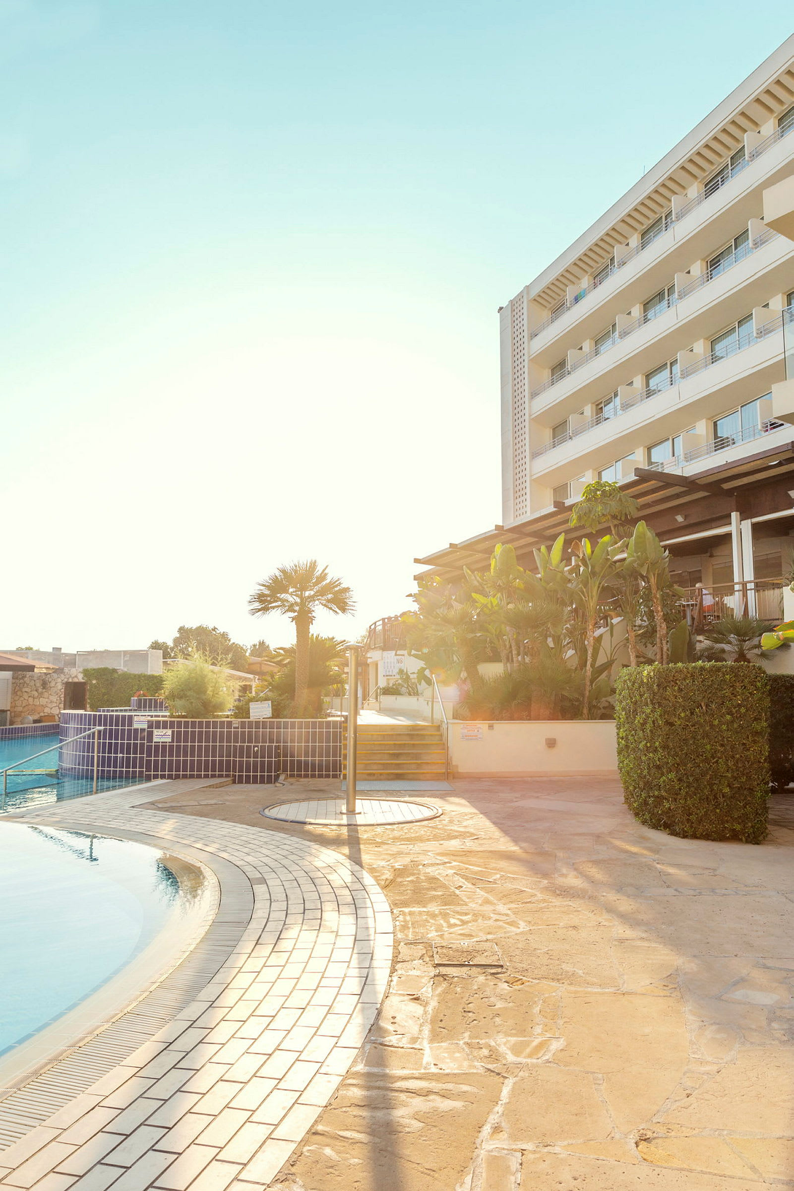 Hotel med poolområde og et anlagt miljø i sollys. (AI-genereret tekst)