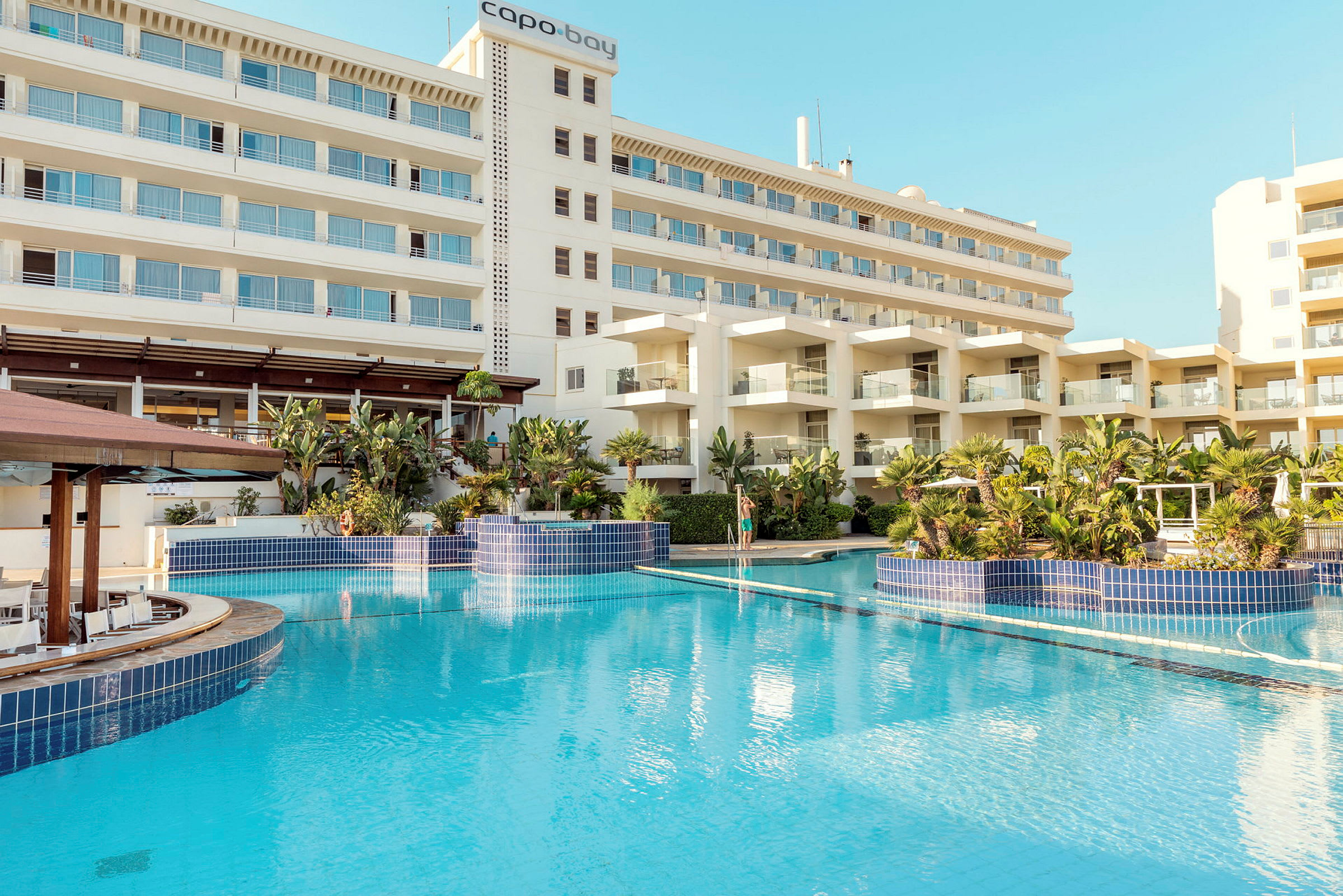 Hotelbygning med flere etager og en stor blå pool omgivet af beplantning. (AI-genereret tekst)