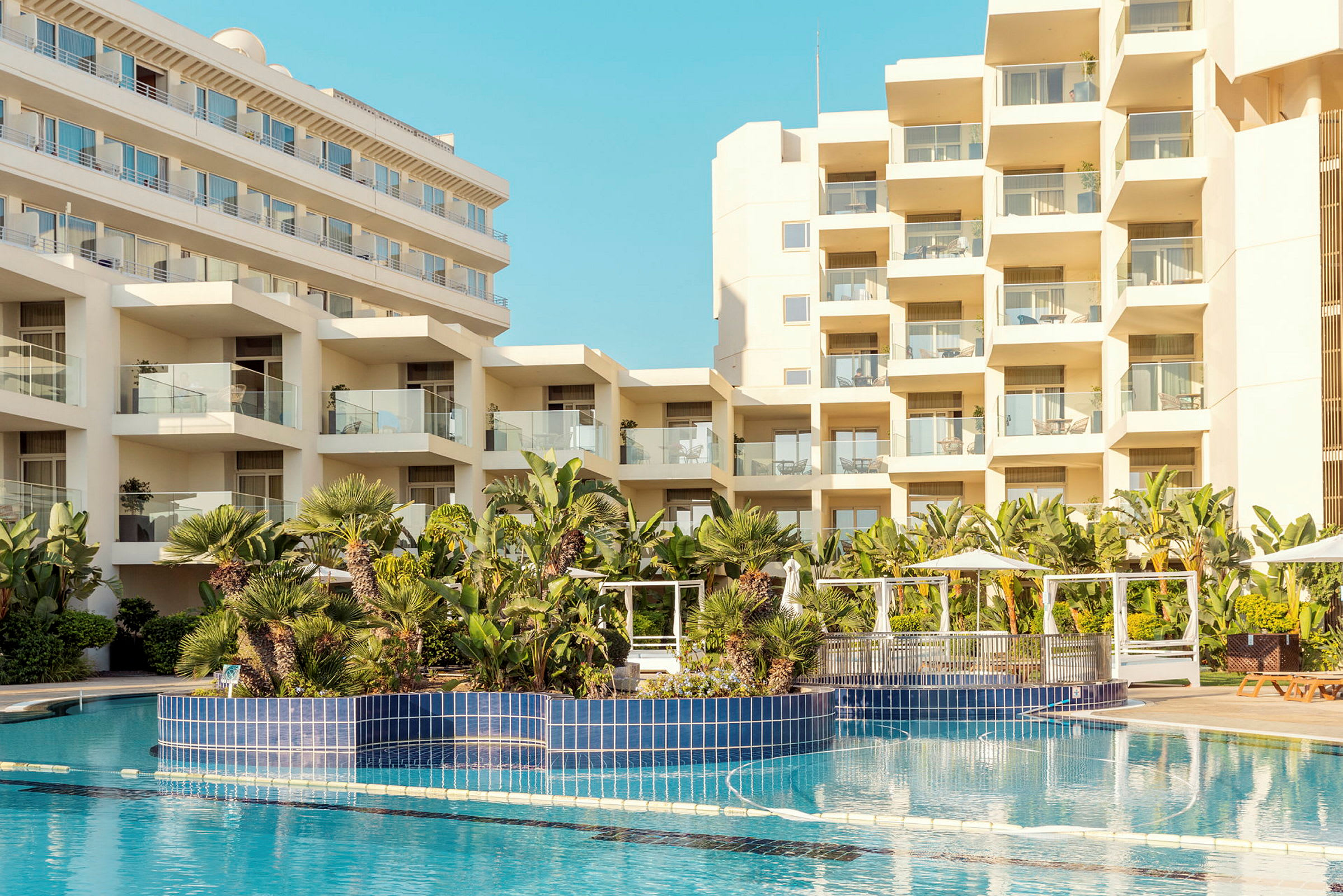 Billede af hotelbygninger med en pool og frodig beplantning i forgrunden. (AI-genereret tekst)