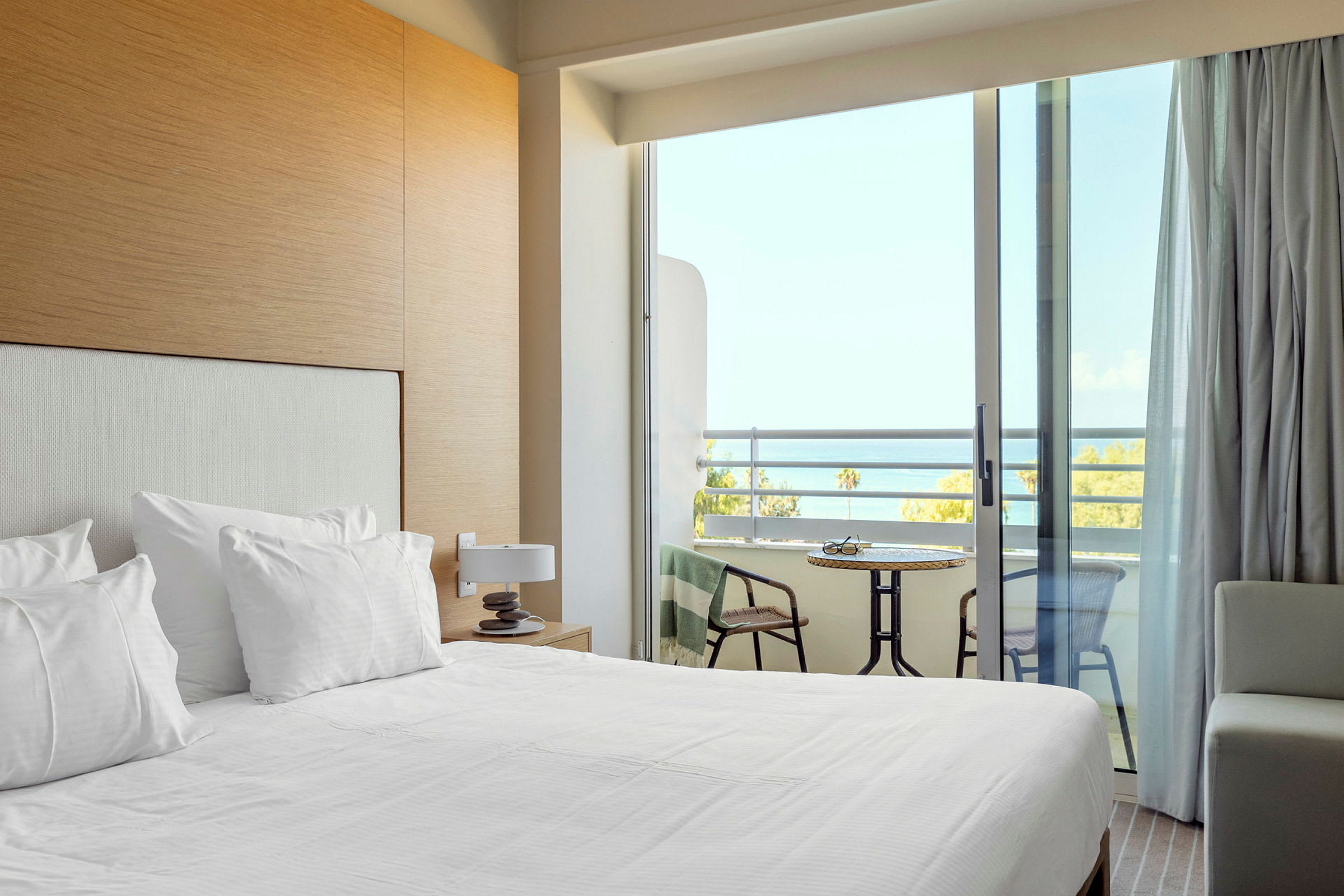 Et hotelværelse med redt seng og en balkon med udsigt over havet. (AI-genereret tekst)