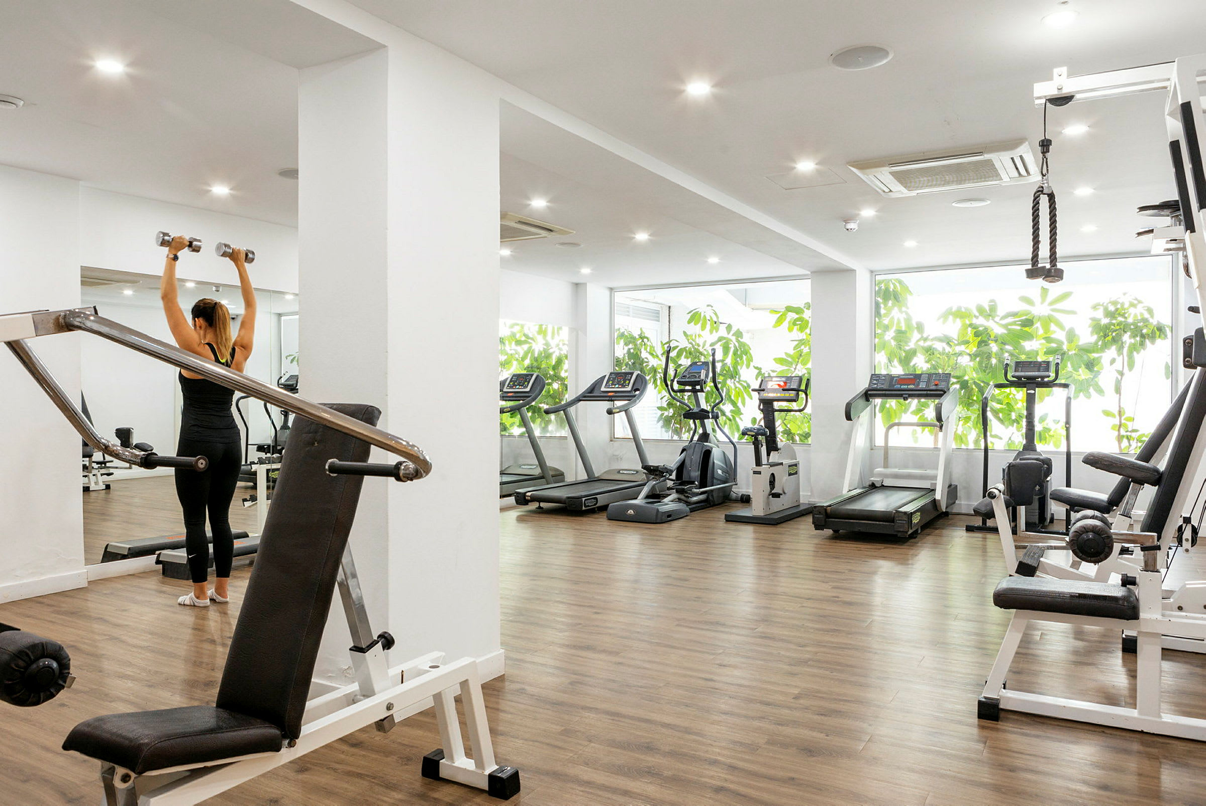 Et fitnesscenter med træningsmaskiner og en person der løfter håndvægte. (AI-genereret tekst)