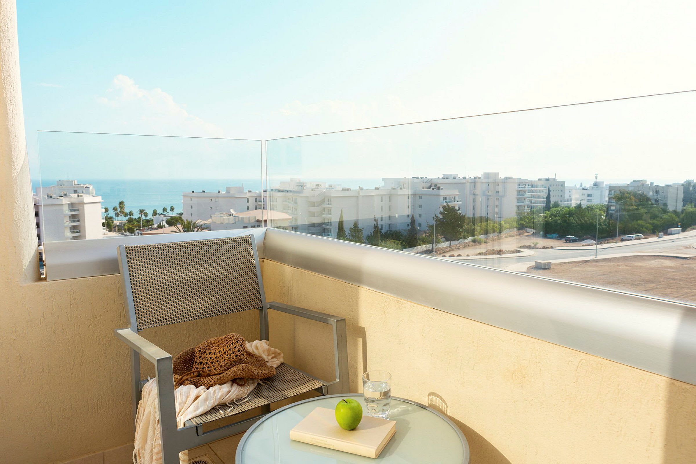 En altan med udsigt over havet og bygningerne, med en stol og et bord med glas, bog og et æble. (AI-genereret tekst)