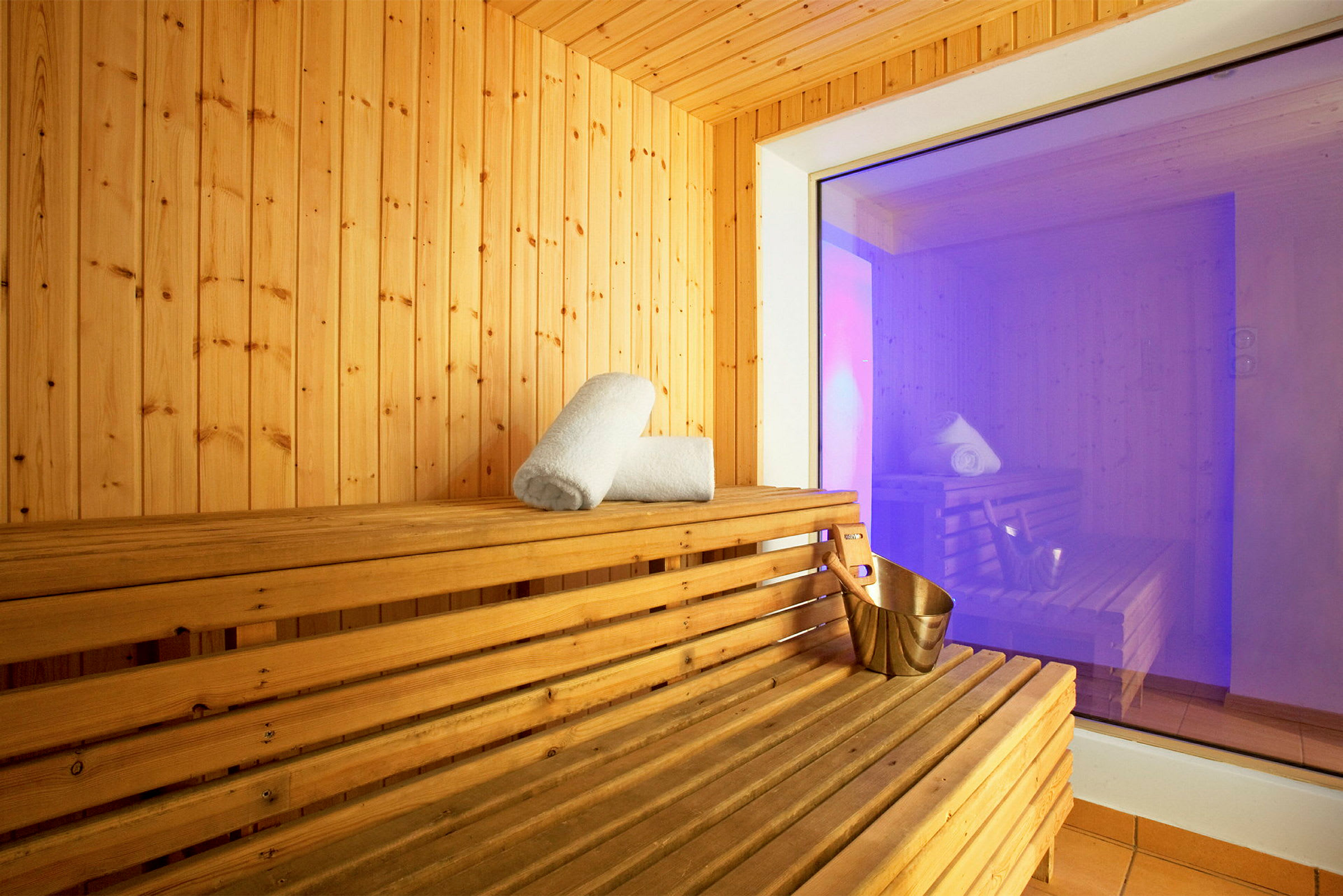 En sauna med trævægge og træbænke. På bænken ligger et sammenrullet håndklæde og en metalskovl. (AI-genereret tekst)