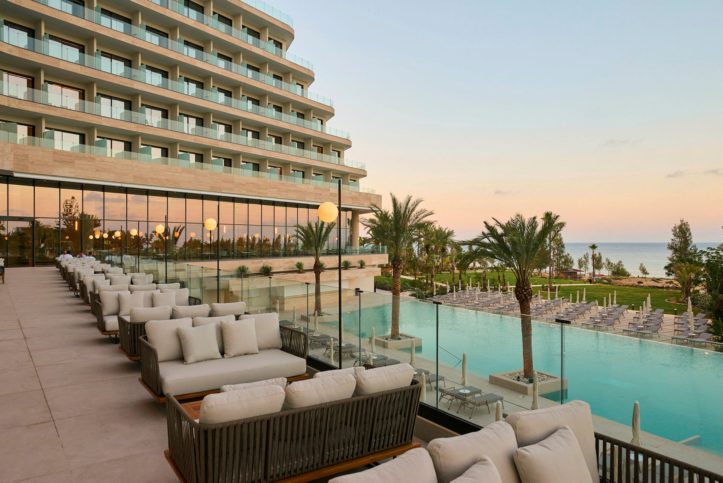 En terrasse med siddeområder med udsigt over en pool og omkringliggende haver, med en moderne bygning i baggrunden. (AI-genereret tekst)
