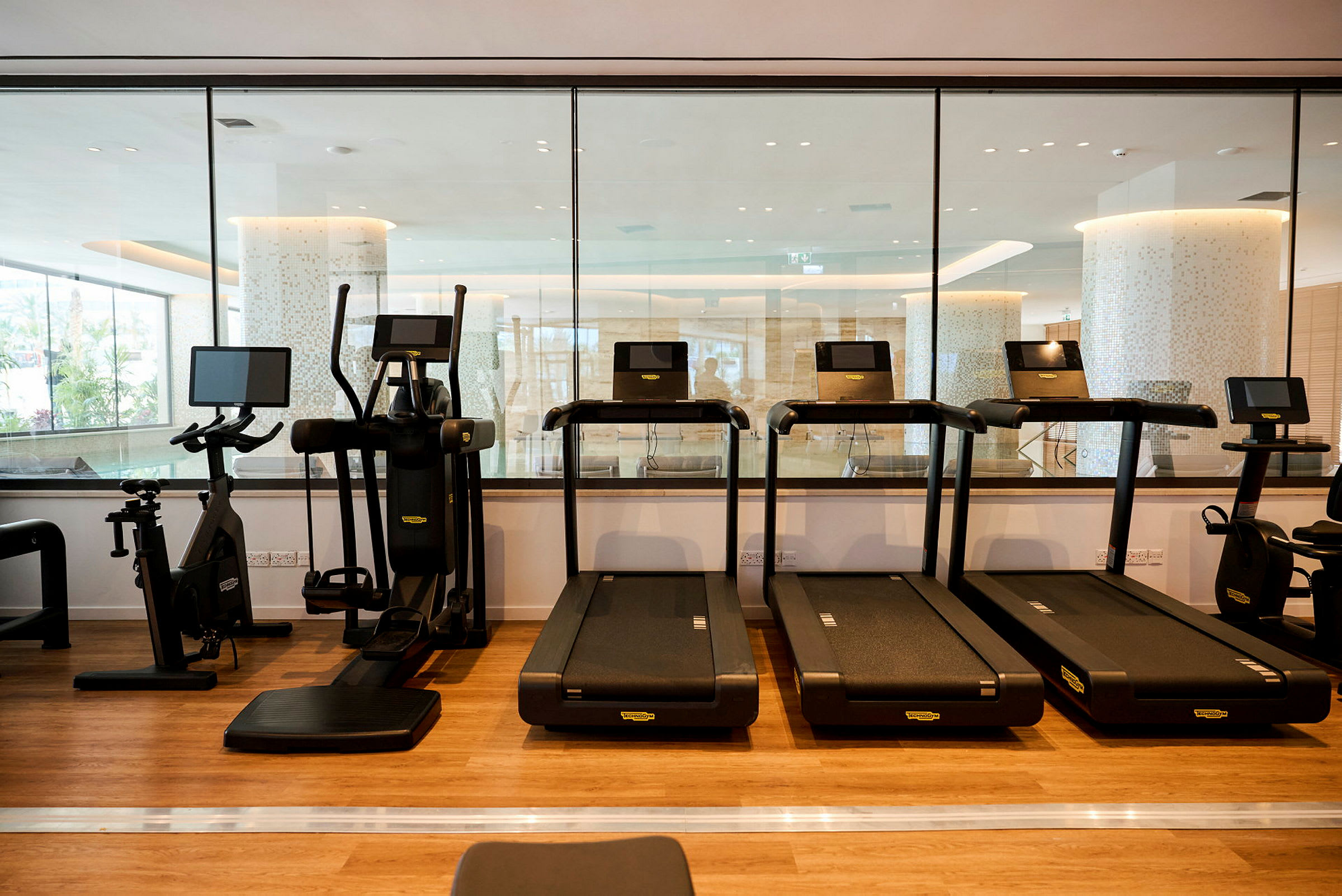 Et fitnesscenter med flere løbebånd og træningsmaskiner på et trægulv. (AI-genereret tekst)