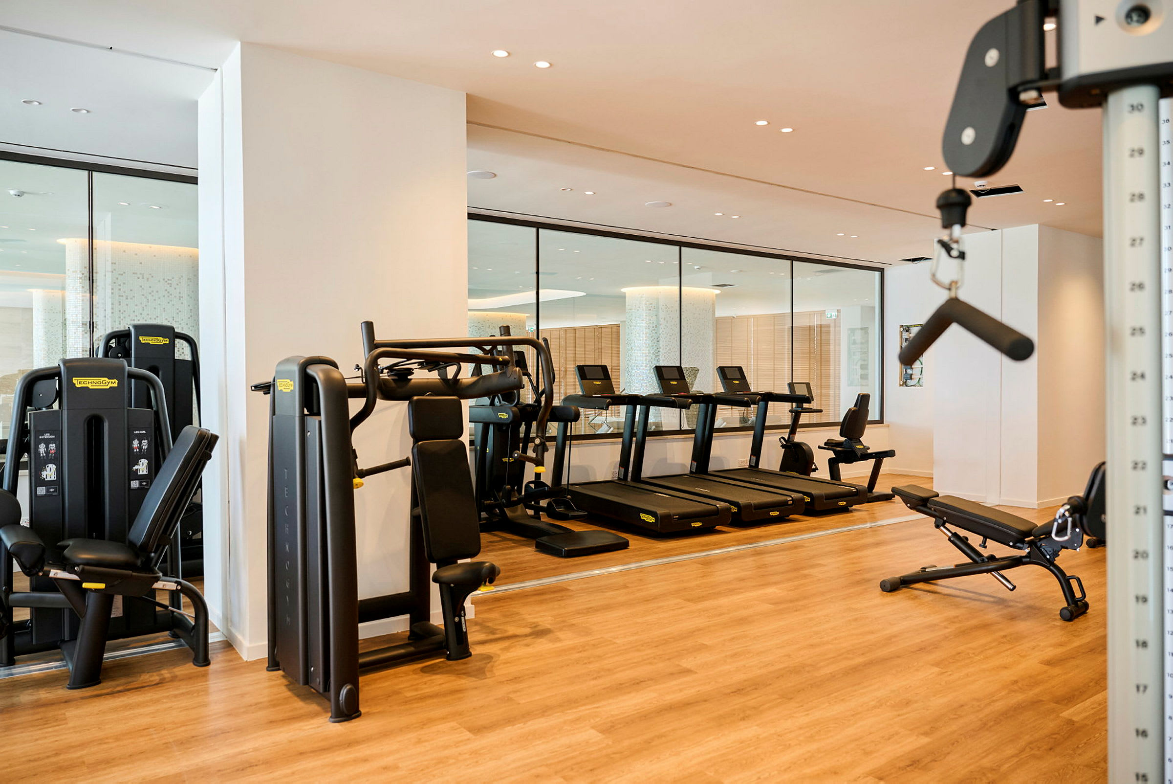 Et moderne fitnesscenter med træningsudstyr såsom løbebånd, styrketræningsmaskiner og bænke på et trægulv. (AI-genereret tekst)