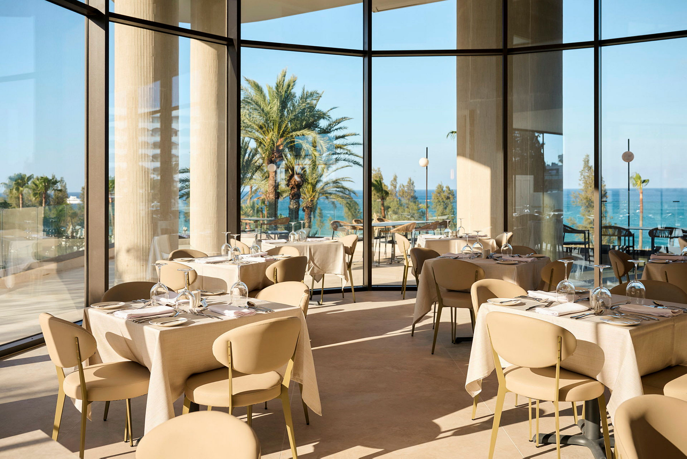 En lys og elegant restaurant med panoramavinduer med udsigt til palmer og hav. (AI-genereret tekst)
