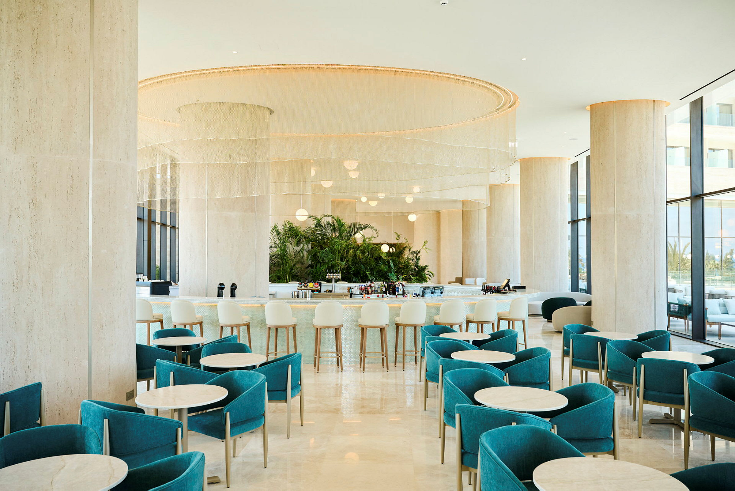 En moderne hotelbar med turkise stole og runde borde, en elegant bardisk i baggrunden og store vinduer, der lukker dagslys ind. (AI-genereret tekst)
