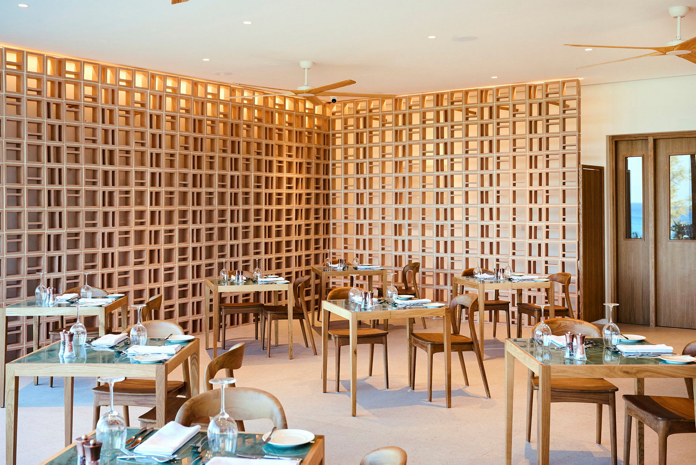 Et moderne restaurantområde med træborde og -stole samt en dekorativ gitterlignende trævæg. (AI-genereret tekst)