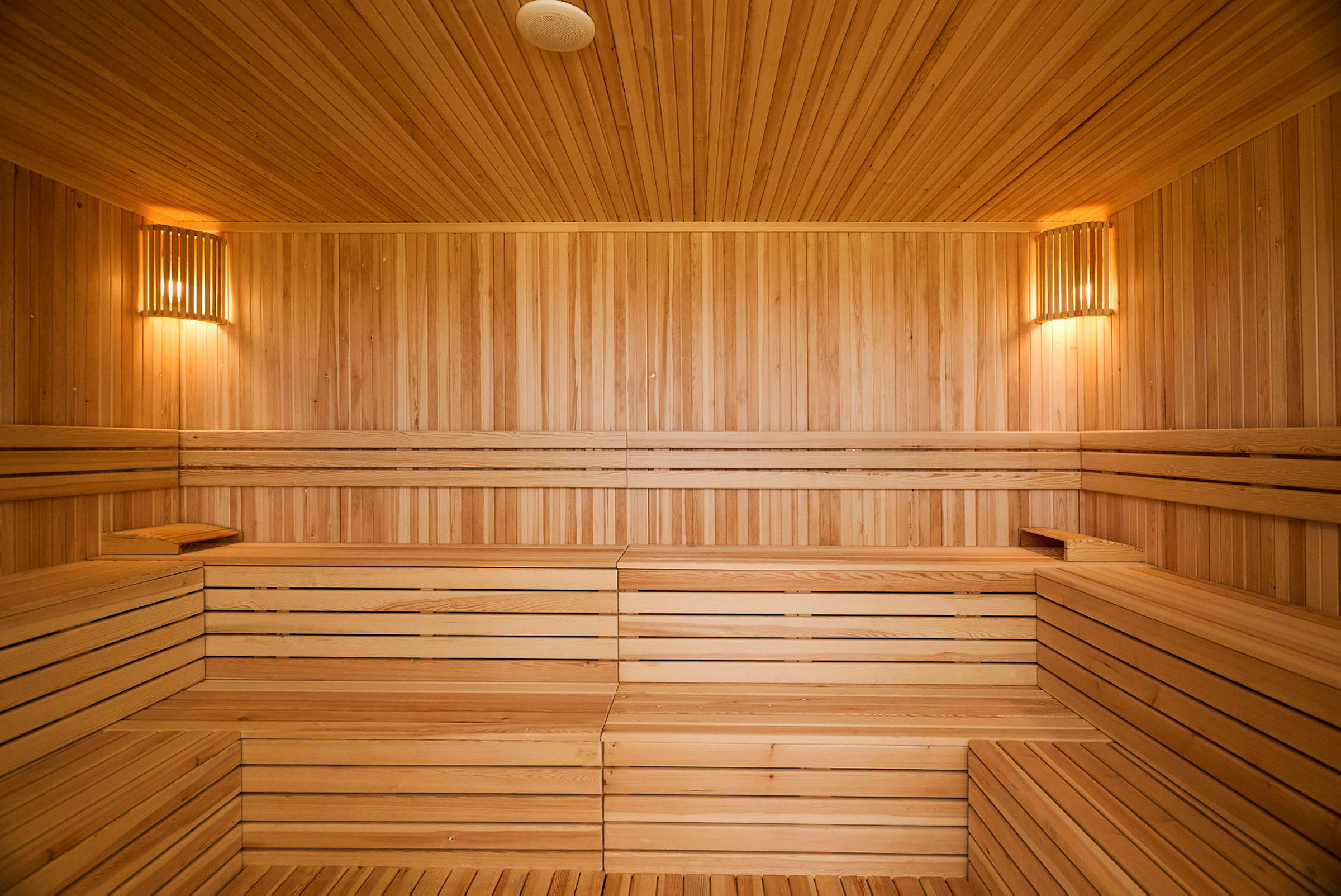 Inde i en sauna med træpanelerede vægge og bænke. Væggene er let oplyst af væglamper. (AI-genereret tekst)
