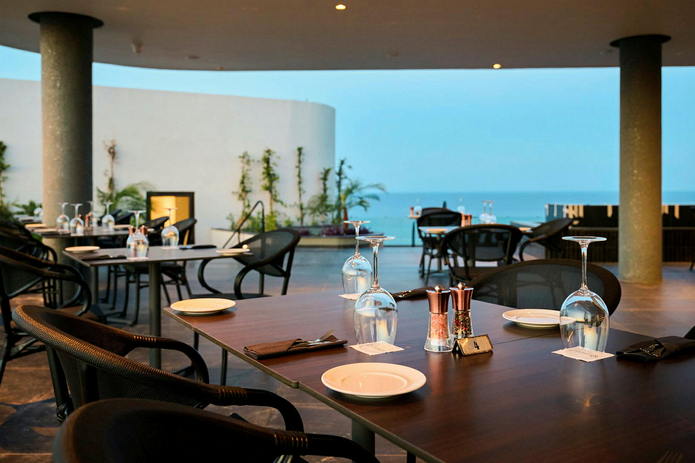 Restaurant med opdækkede borde på en terrasse med udsigt over havet. (AI-genereret tekst)