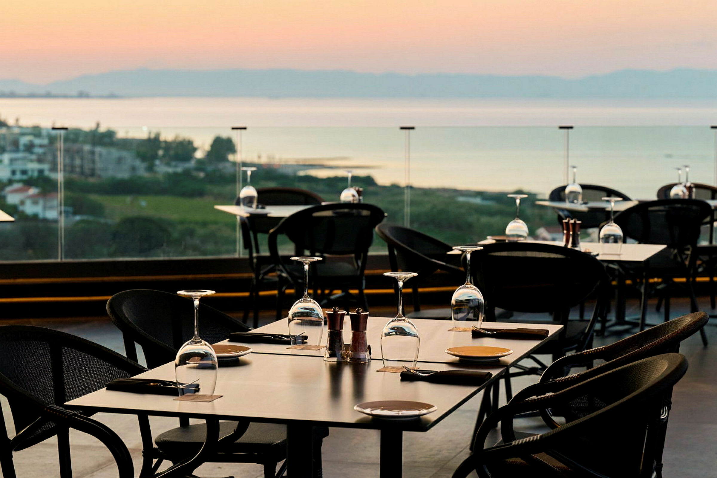 En udendørsrestaurant med dækkede borde og udsigt over landskab og vand. (AI-genereret tekst)