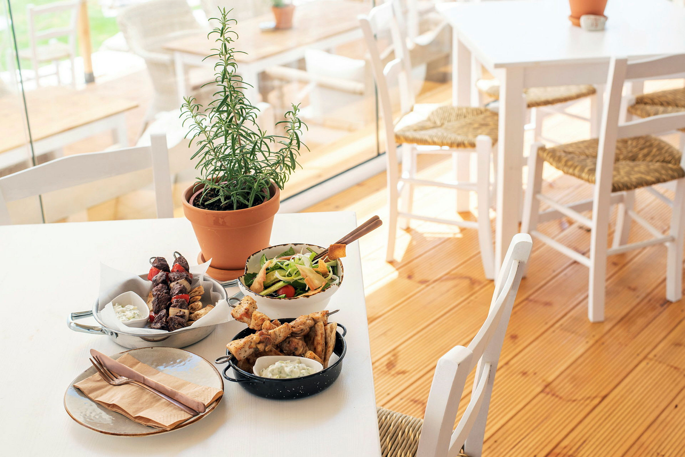Et dækket bord med forskellige retter, inklusiv salat, grillspyd og en urteplante. (AI-genereret tekst)