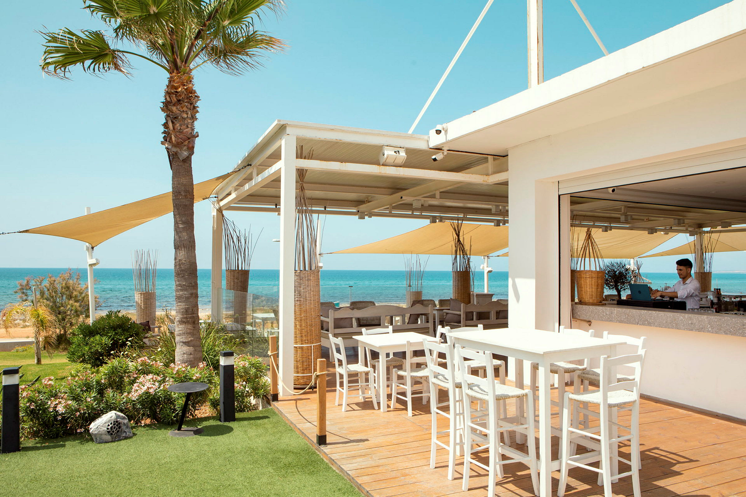 En udendørsrestaurant med borde og stole, udsigt over havet og klar blå himmel. (AI-genereret tekst)