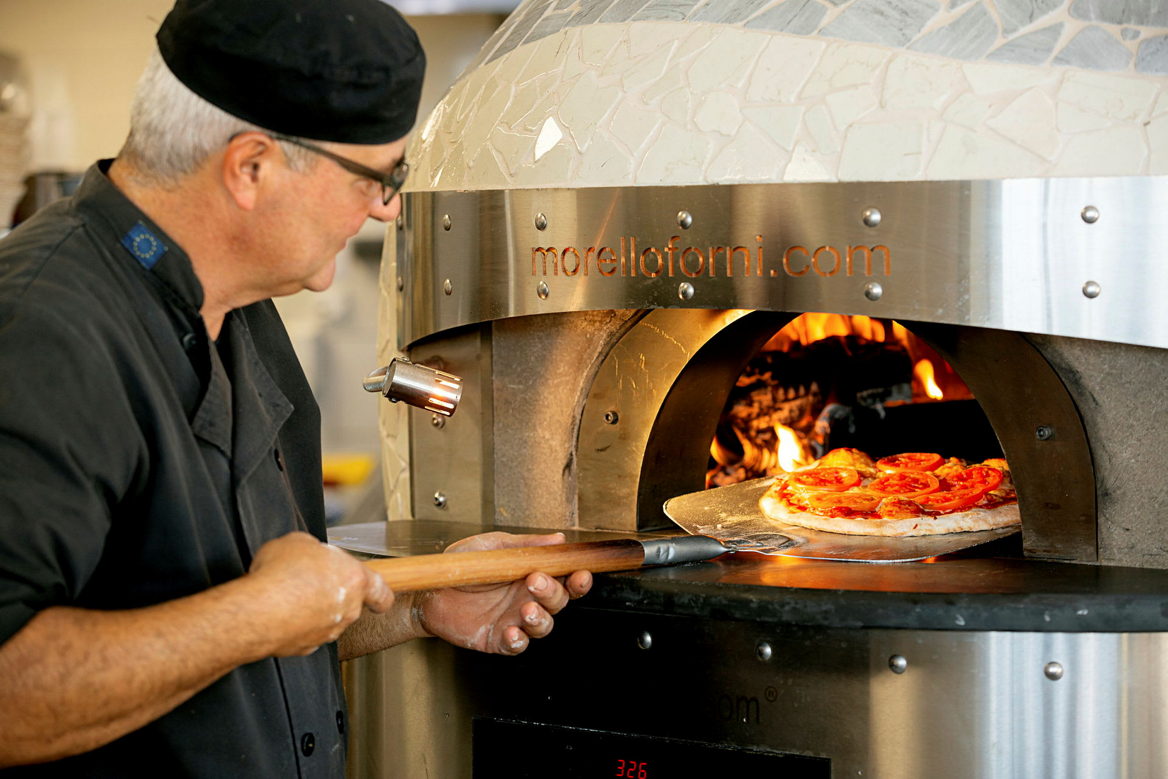 En pizza placeres i en brændefyret ovn med en pizzaspade. (AI-genereret tekst)