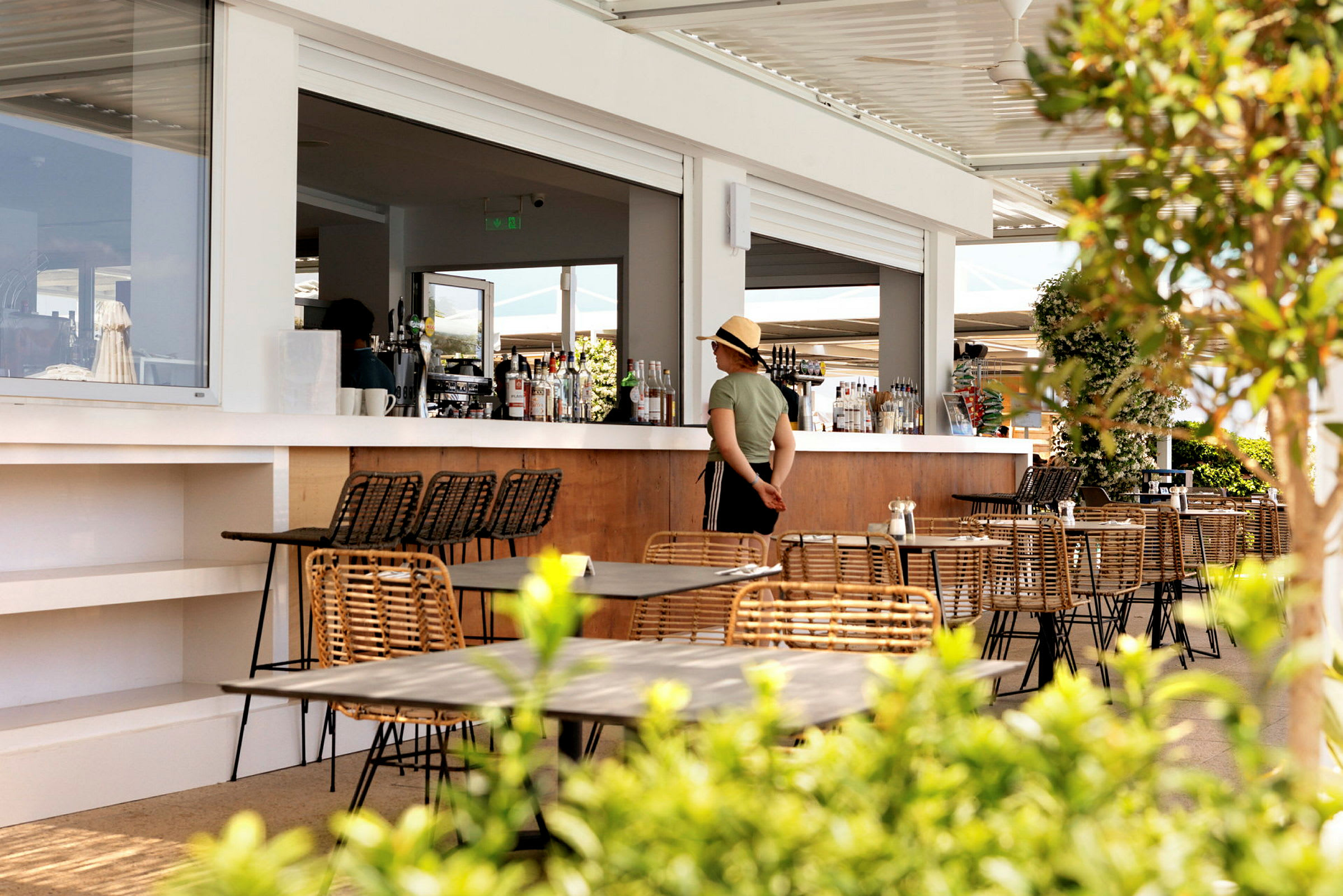 Udendørs serveringsområde med borde og stole og en bar i baggrunden. (AI-genereret tekst)