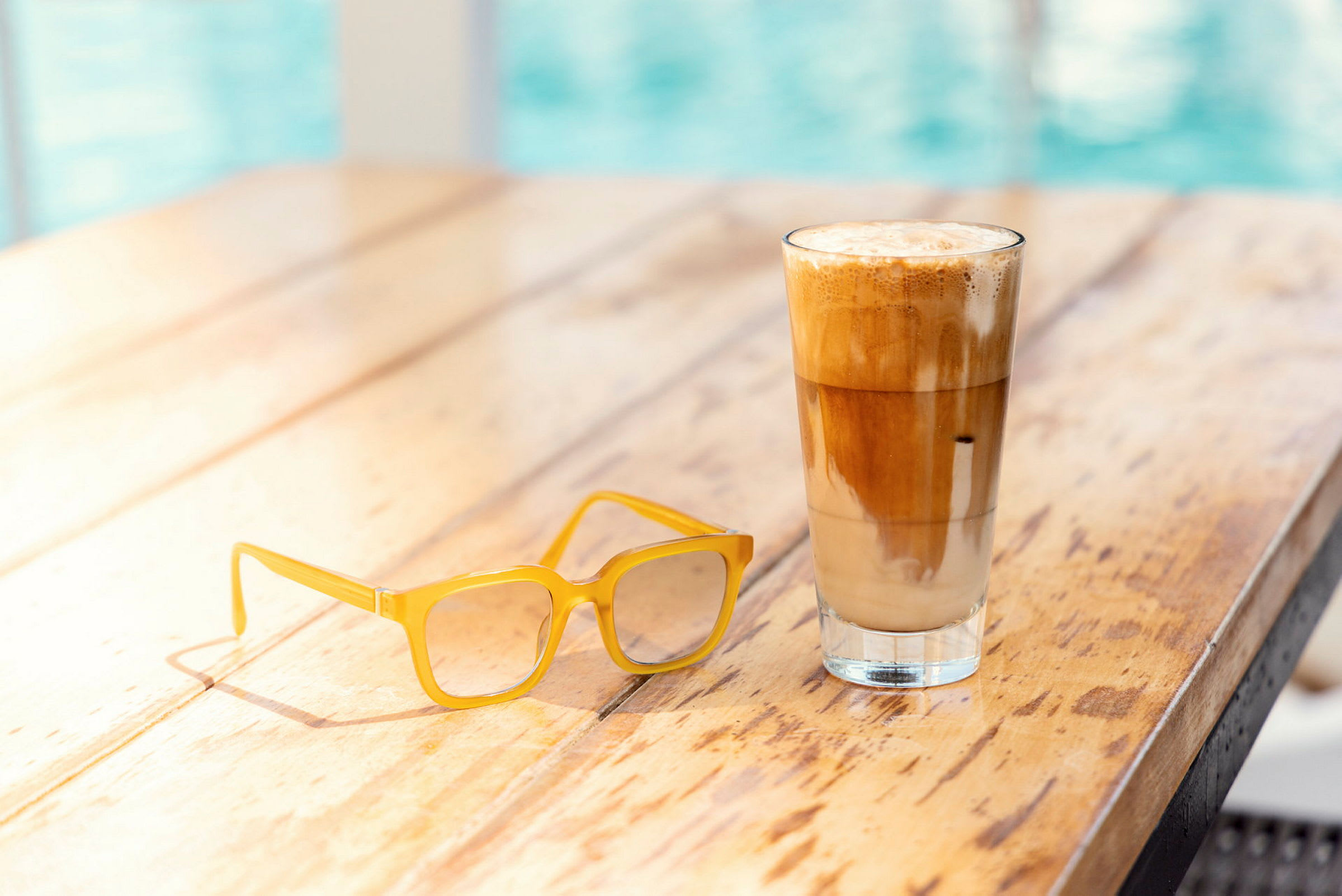 Et træbord med et par gule briller og et glas iskaffe eller latte. (AI-genereret tekst)
