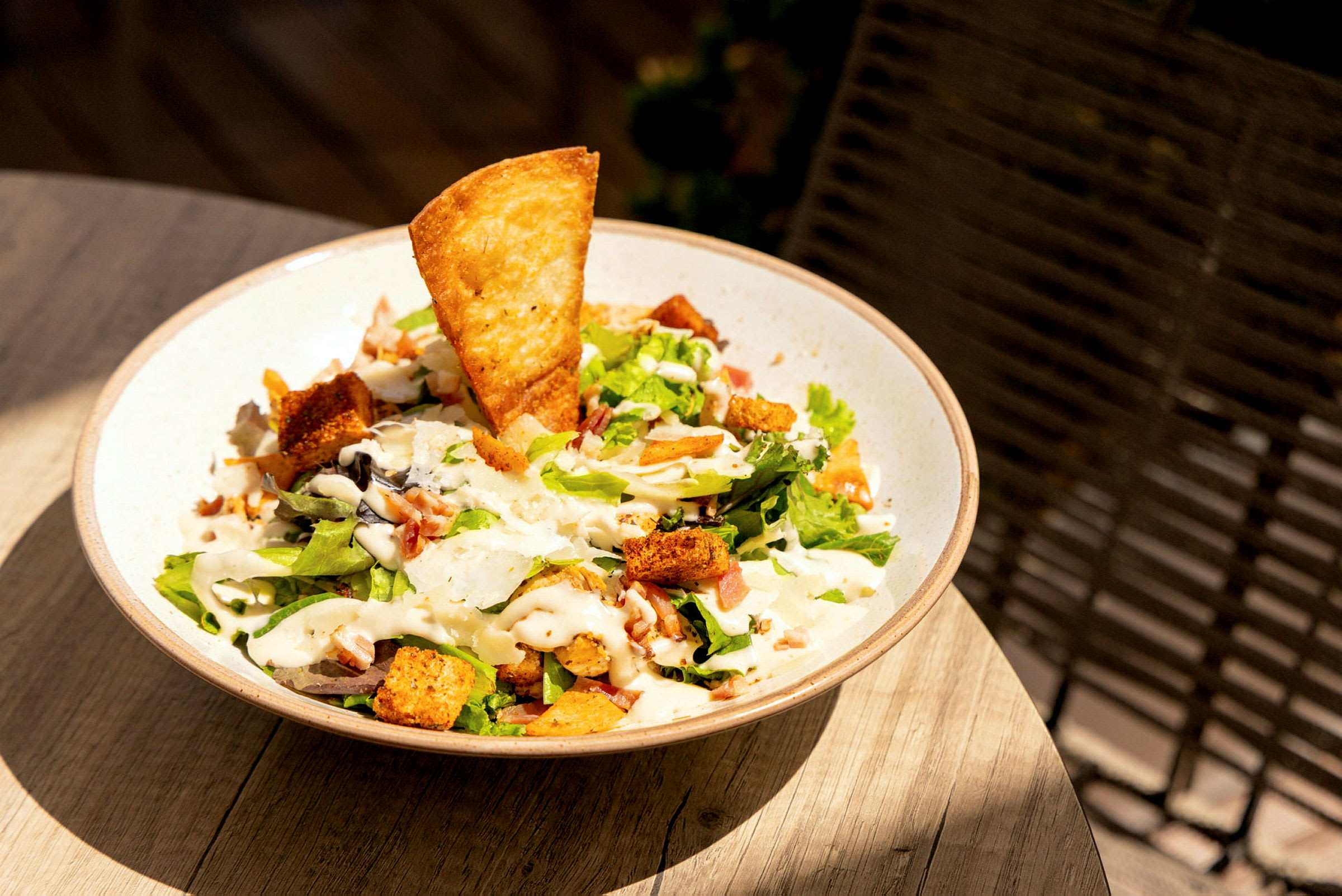En skål med salat, der indeholder grøntsager, croutoner, et sprødt brød og dressing. (AI-genereret tekst)