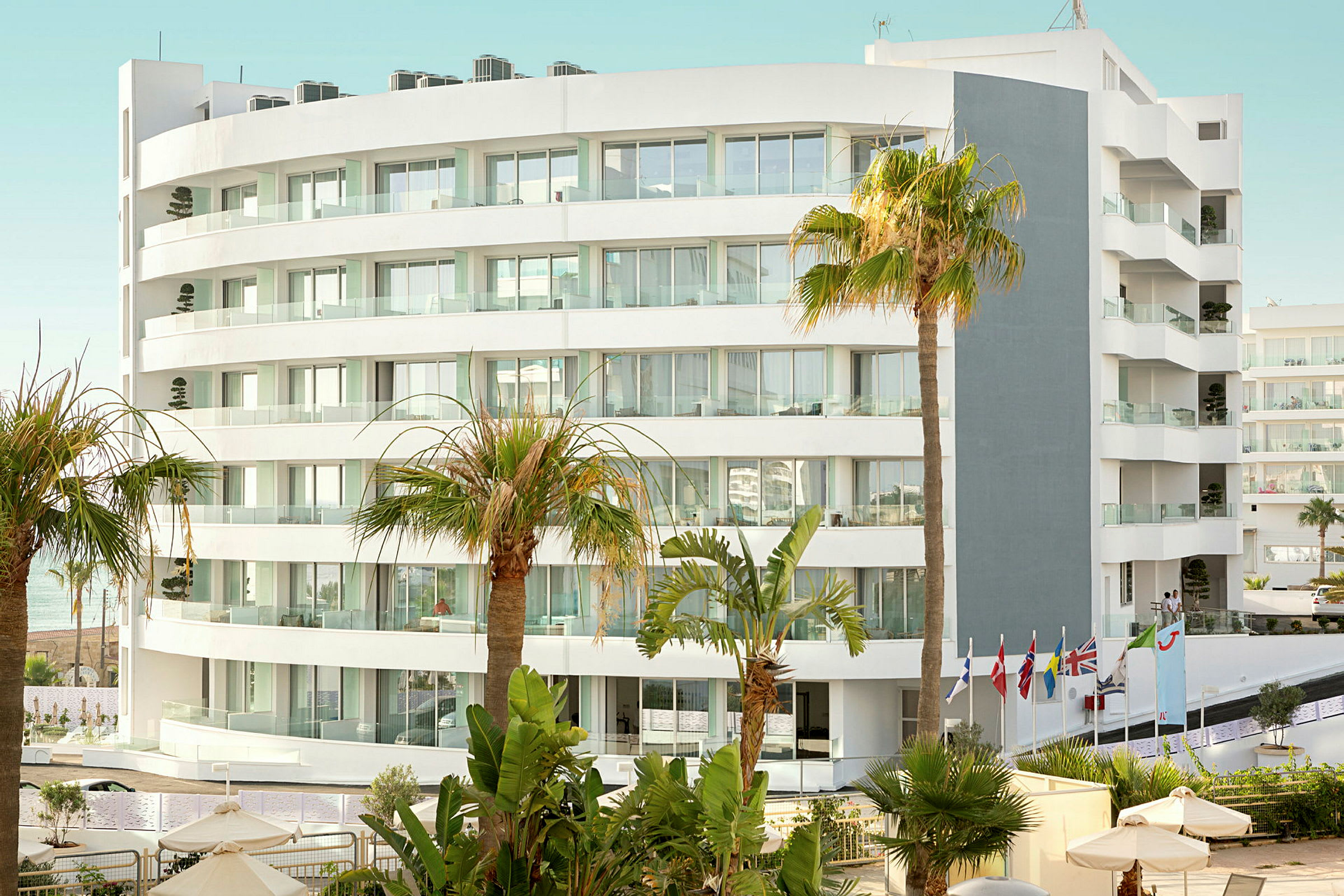 Billede af en moderne hvid hotelbygning omgivet af palmer og vegetation. (AI-genereret tekst)