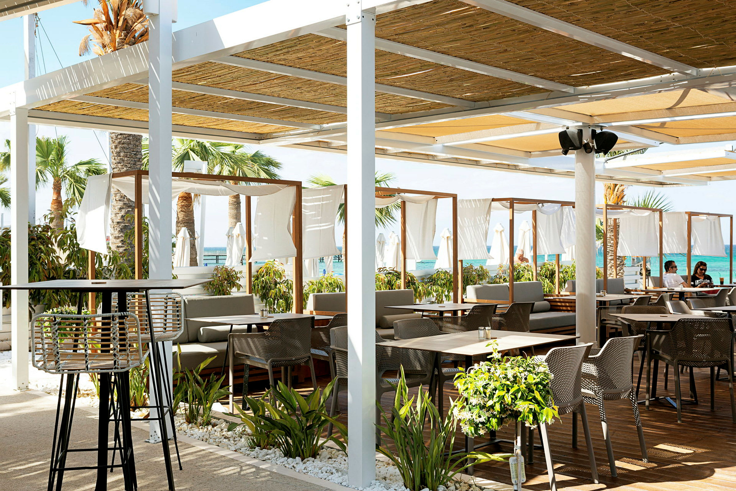 Strandnær restaurant med udendørsmøbler og dekorativ beplantning. (AI-genereret tekst)
