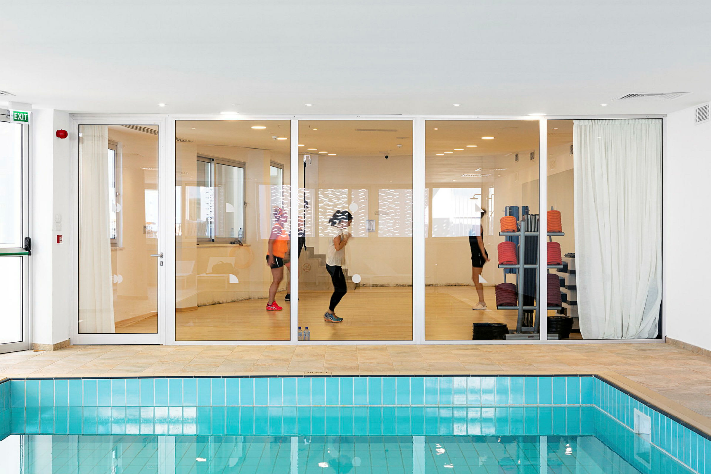 Glasdøre til et fitnesscenter med personer, der træner, set fra et rum med en pool. (AI-genereret tekst)