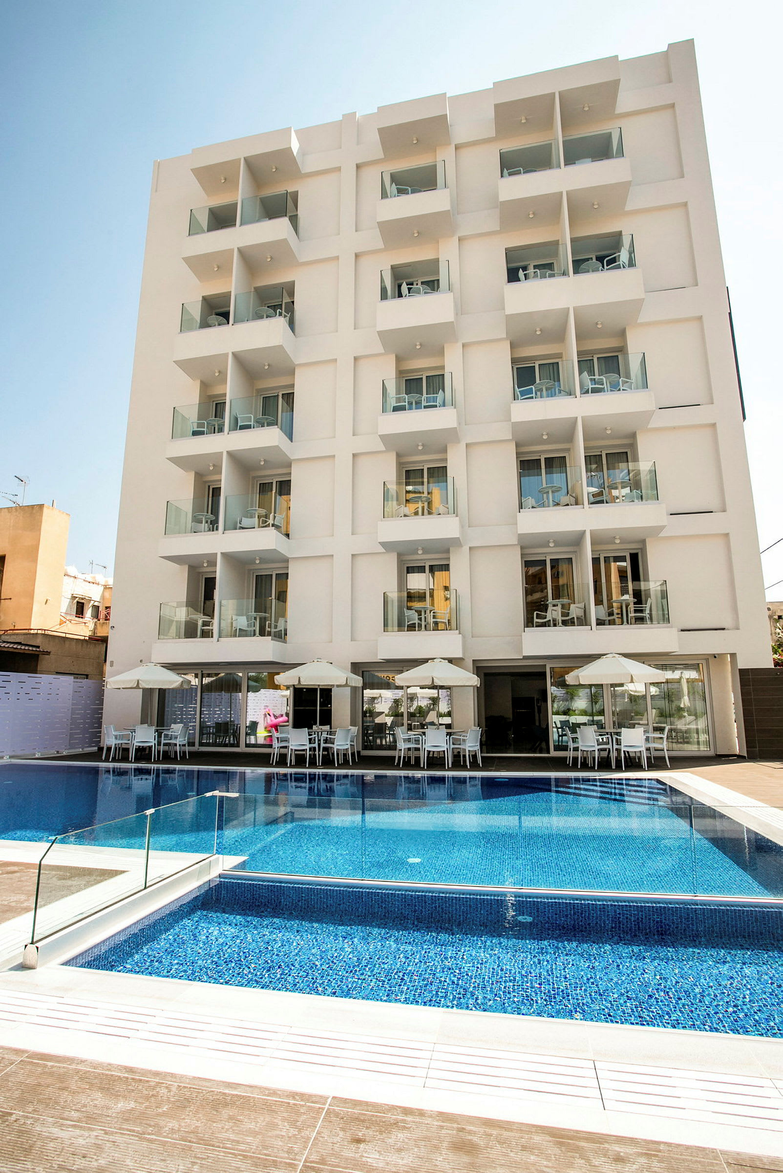 Billede af et moderne hotel med flere altaner og en pool foran. (AI-genereret tekst)