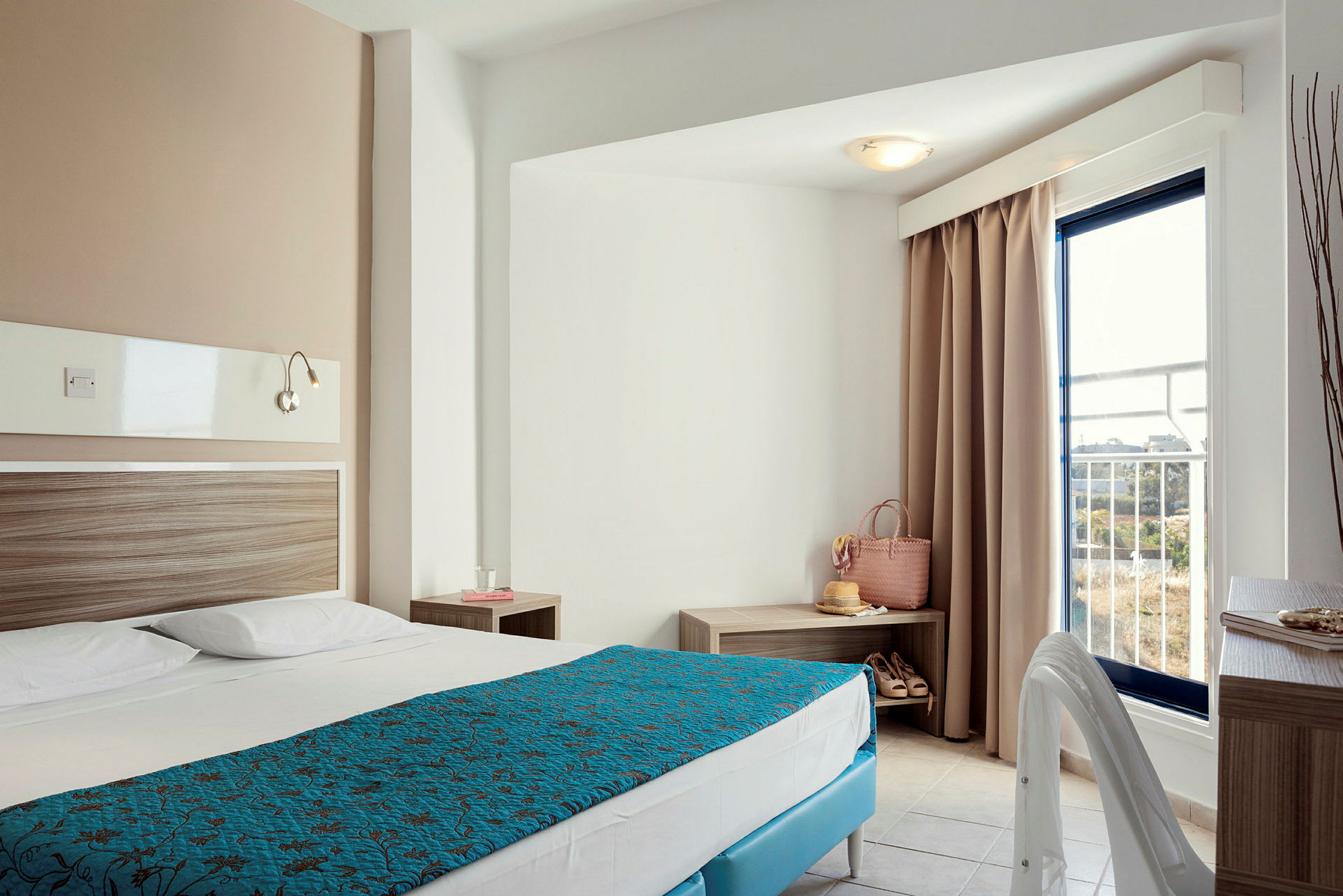 Hotelværelse med en opslået seng, natbord og en altandør. (AI-genereret tekst)